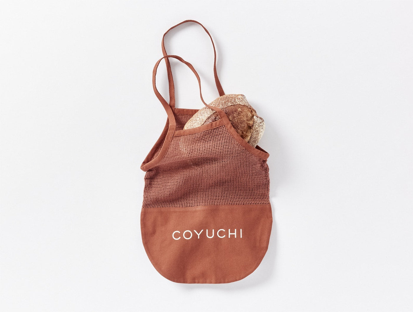 Coyuchi Conserve tote bag in terracotta mesh with canvas base, filled with bundled linens.