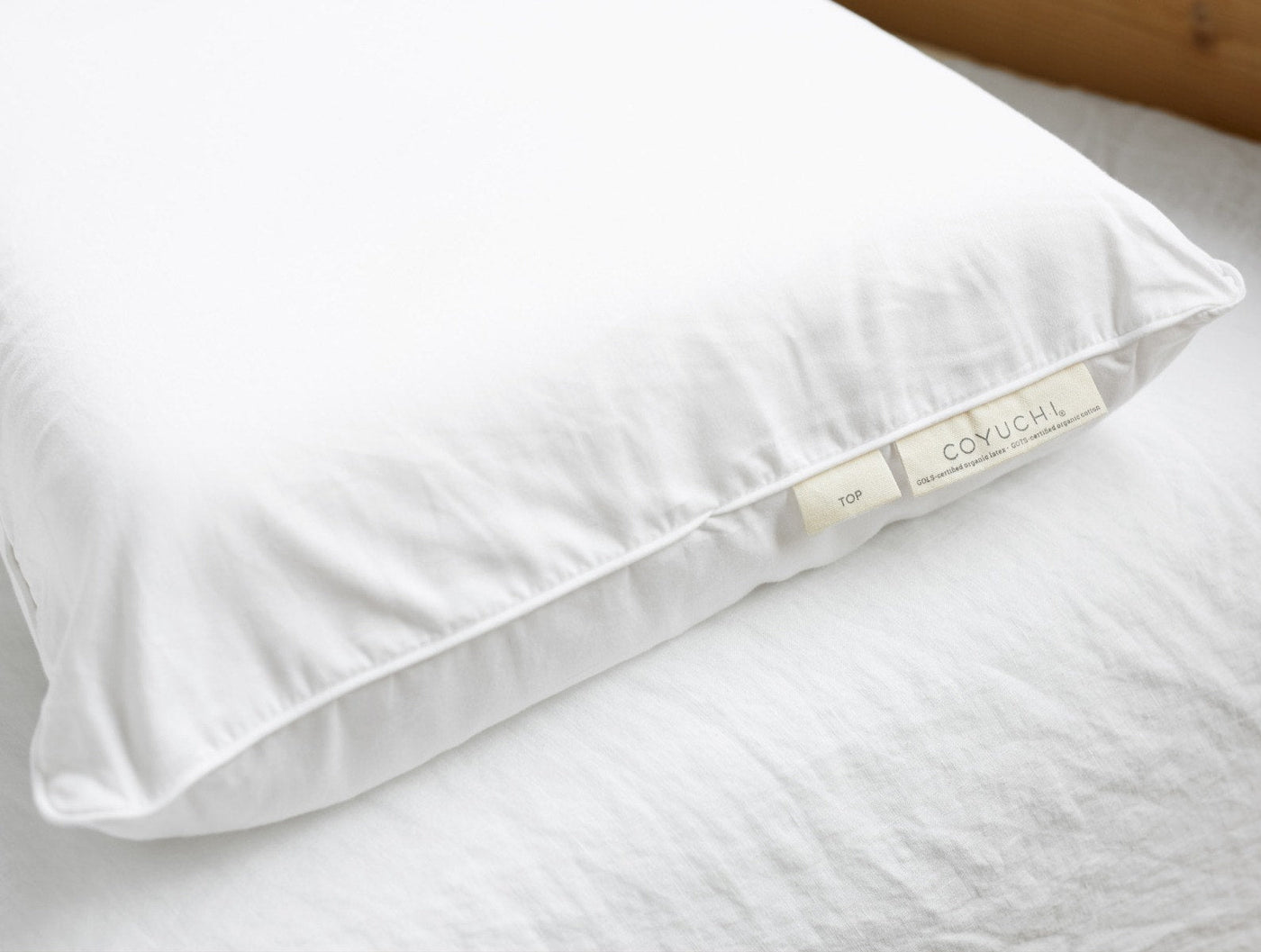 Close-up of Coyuchi Turiya Latex pillow in white with visible label, on linen bedding.