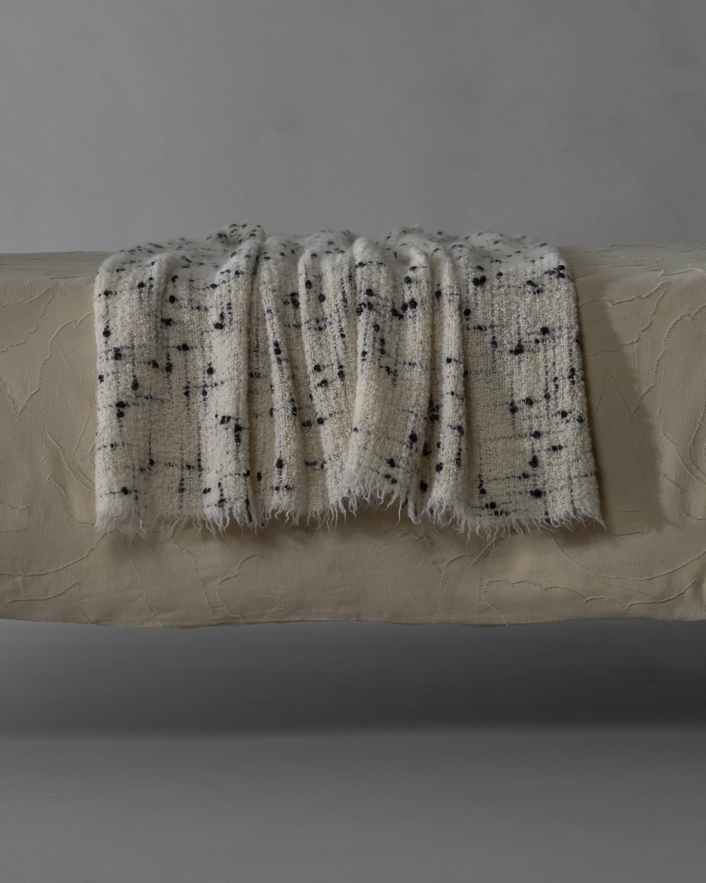 Society Limonta Peg ivory boucle throw with dark speckled pattern and fringe edges draped on bench.