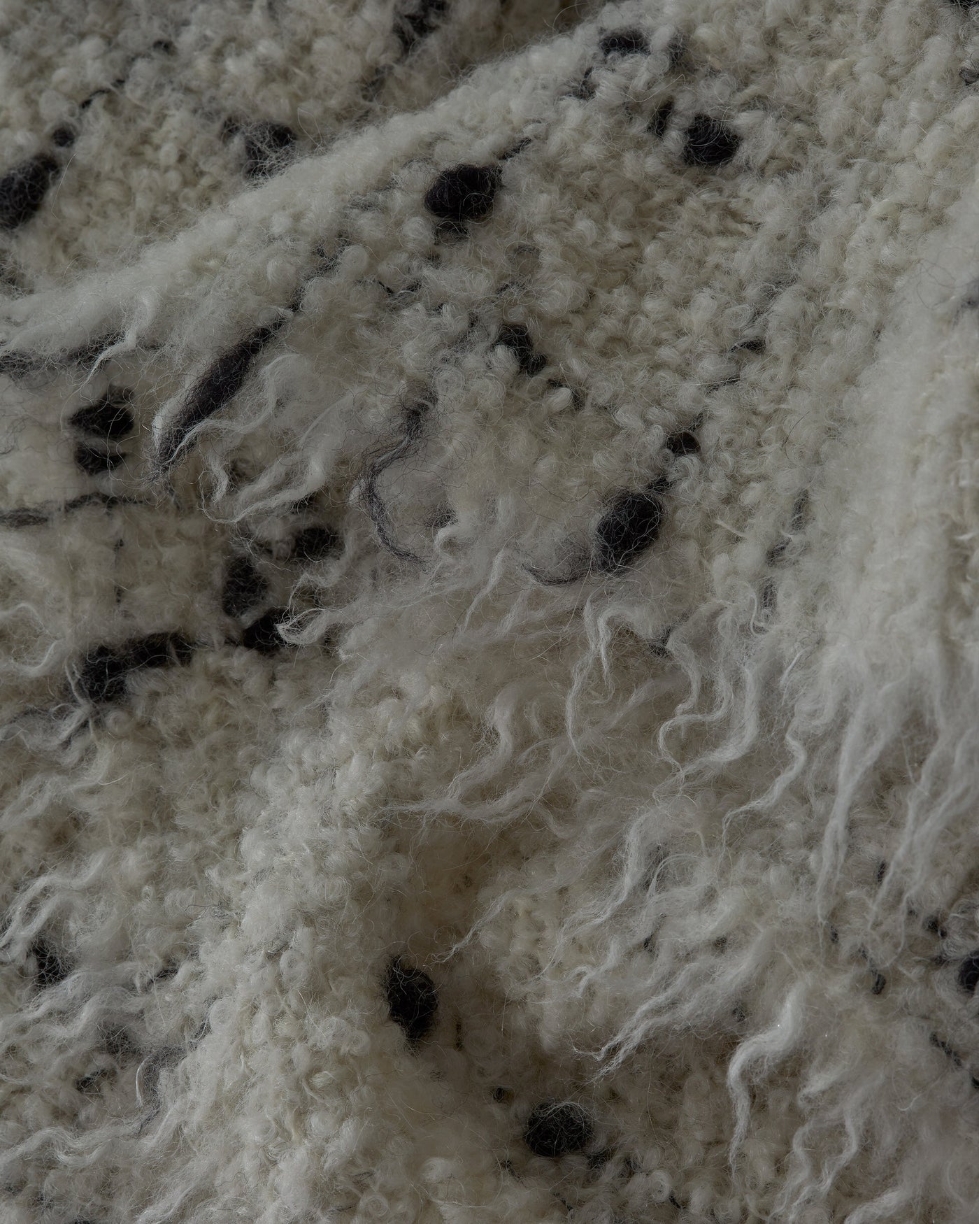 Close-up of Society Limonta Peg throw's ivory boucle texture with scattered charcoal fleck detail.