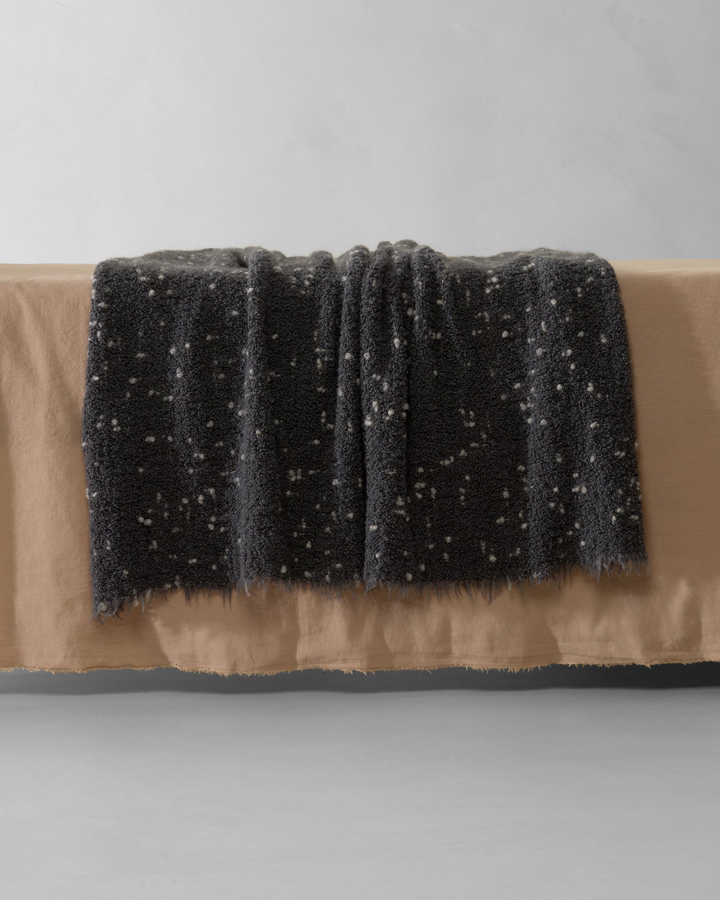 Close-up of Society Limonta Peg throw in charcoal with flecked texture, draped over a bench.