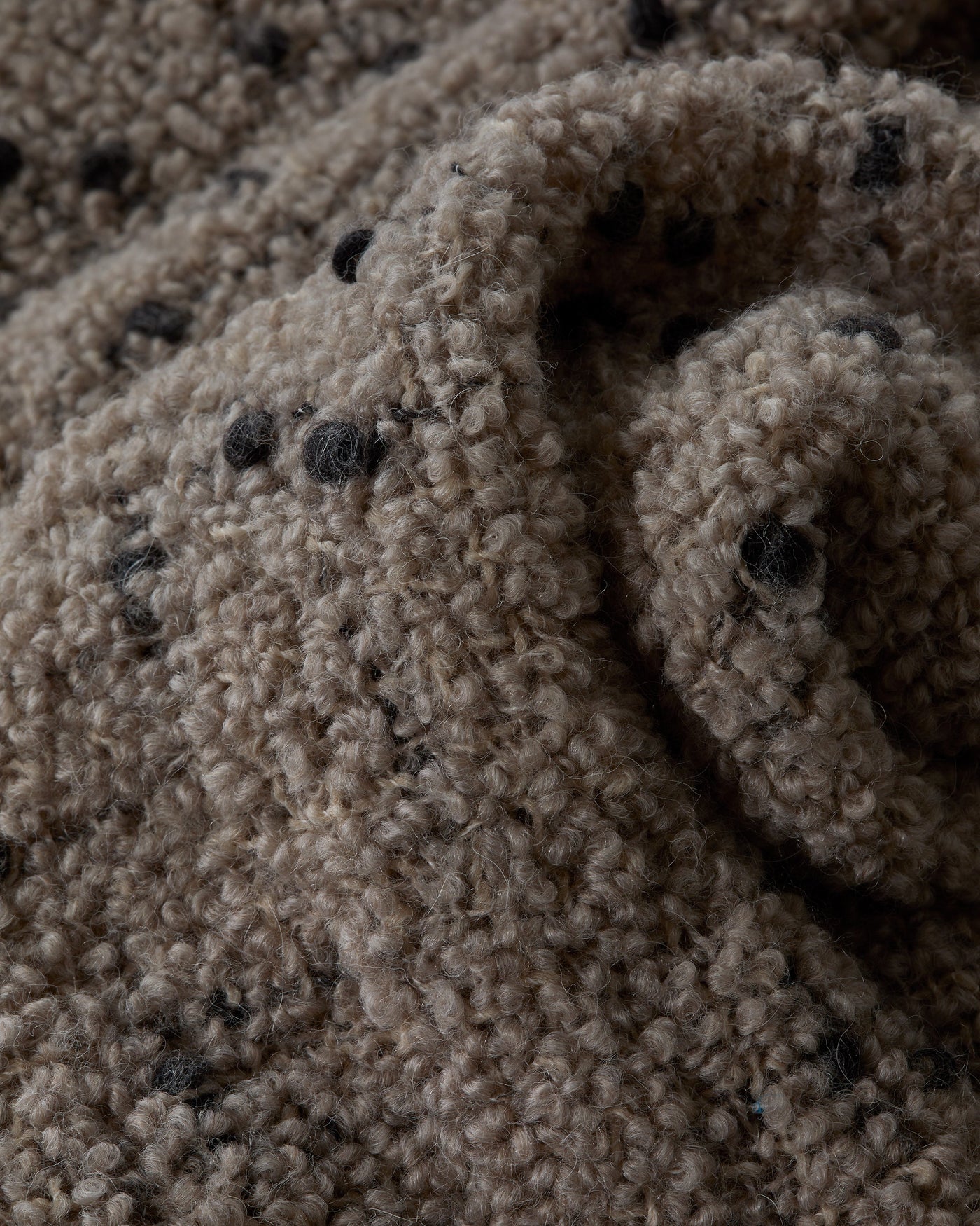 Close-up of bouclé texture with charcoal fleck detail on a taupe wool throw.