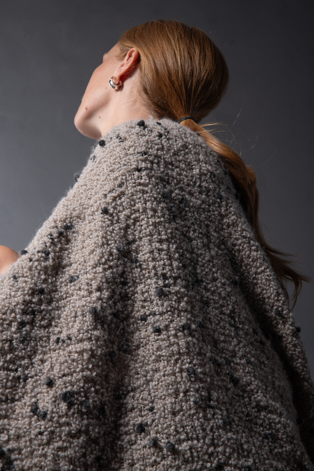 Close-up of Society Limonta Peg throw draped over shoulders, showing stone boucle texture with dark flecks.