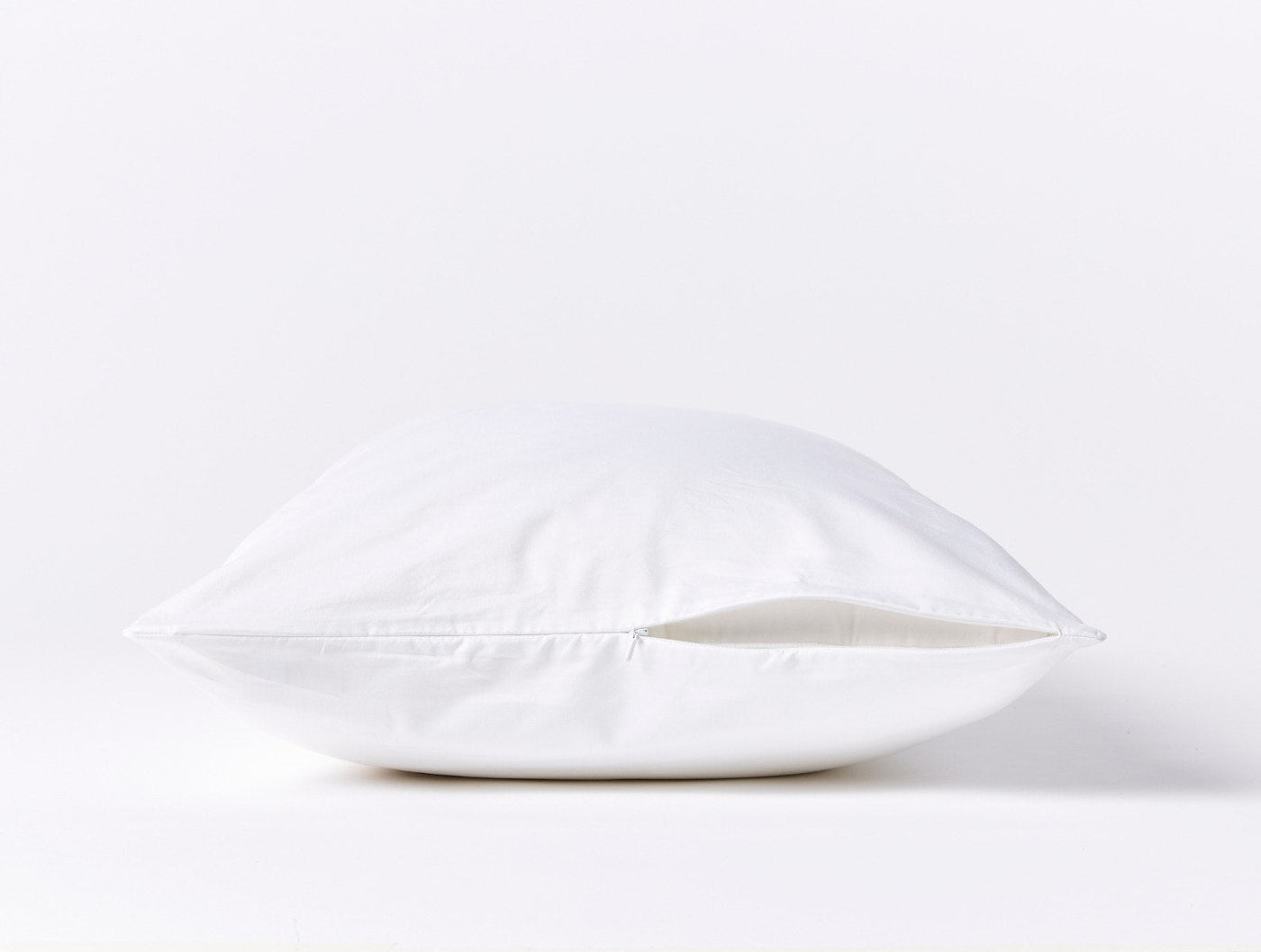 Side profile view of white Coyuchi pillow protector showing zipper closure detail.