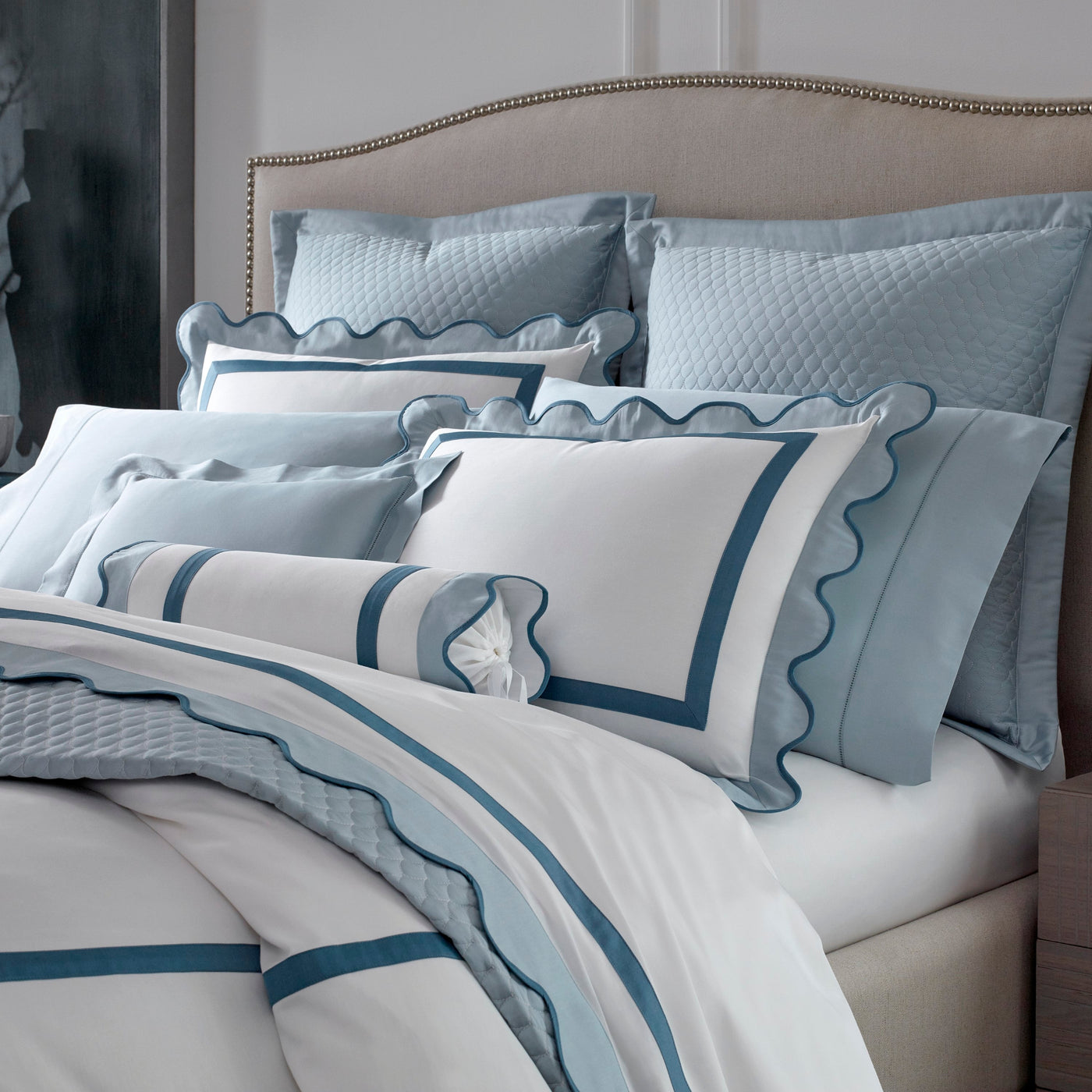 Close-up of Portofino bedding in white with dusty blue scalloped trim and coordinating pillows.