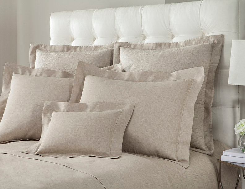Layered champagne linen pillow arrangement on a tufted white headboard.