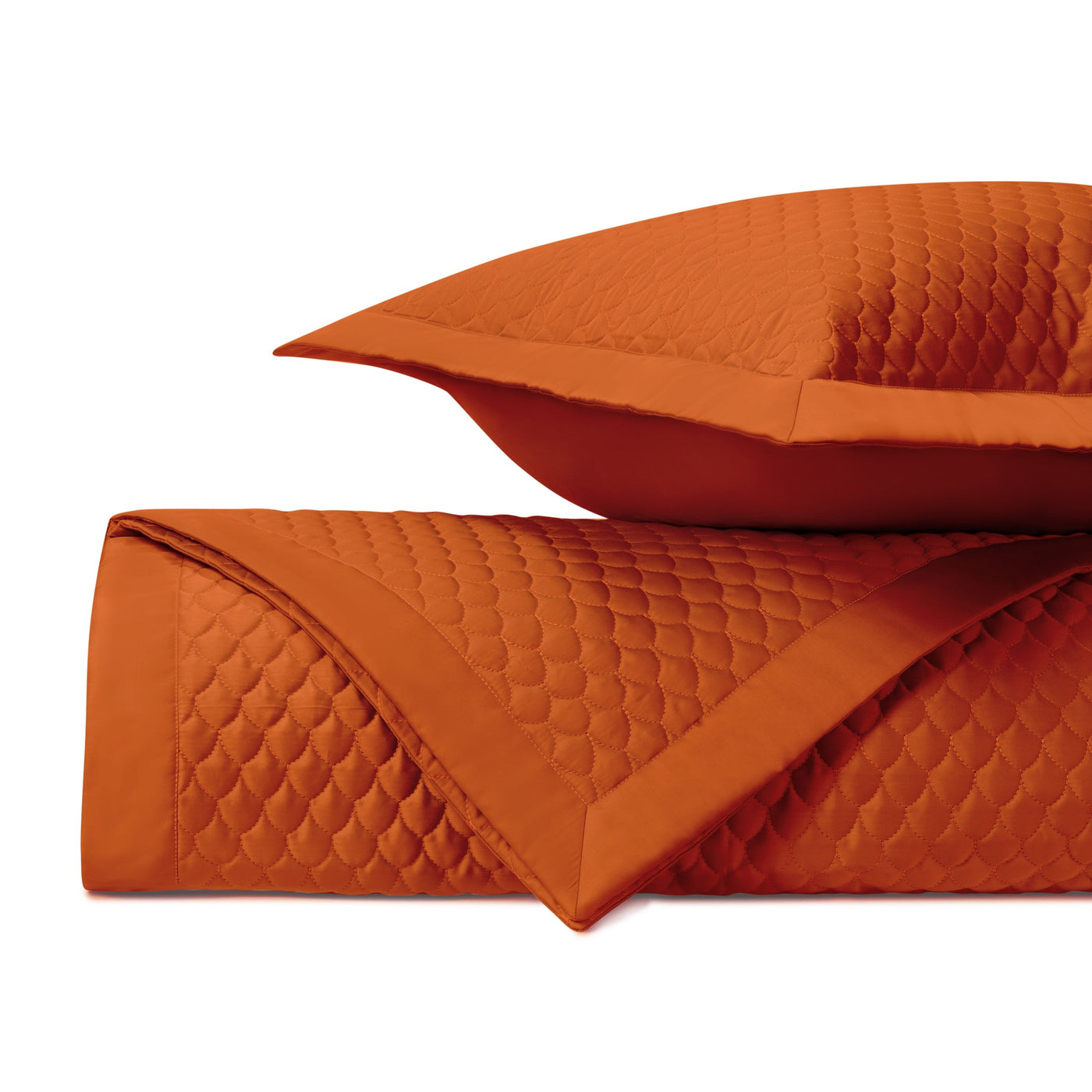 Close-up of tangerine quilted raindrop-pattern coverlet and sham edge detail.