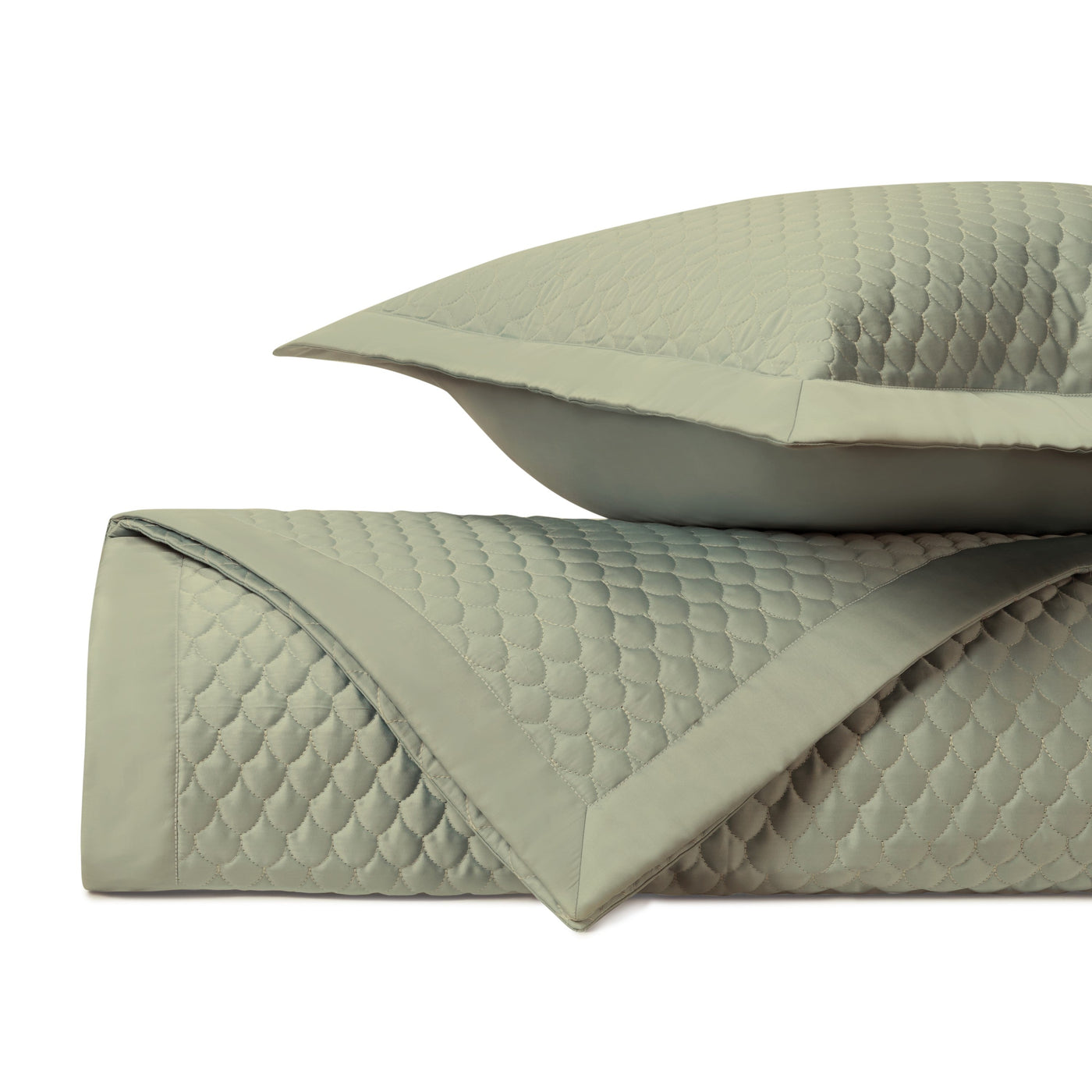 Close-up of sage green quilted coverlet and sham with scallop stitching pattern and border trim.