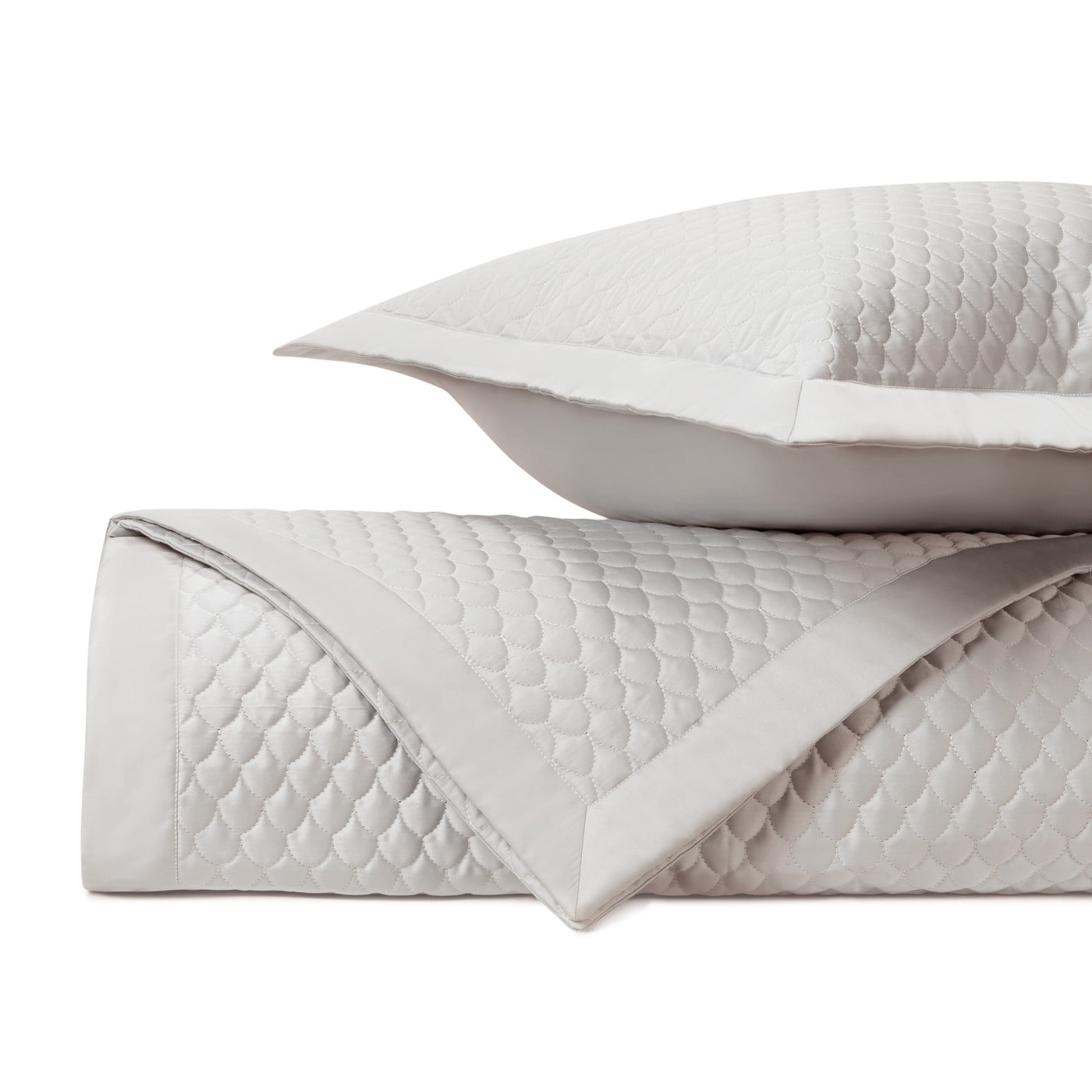Close-up of ivory quilted raindrop-pattern coverlet with satin border and matching sham.