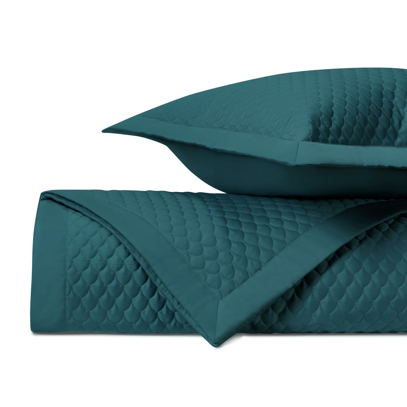 Close-up of teal quilted raindrop-pattern coverlet and sham, folded to show texture.