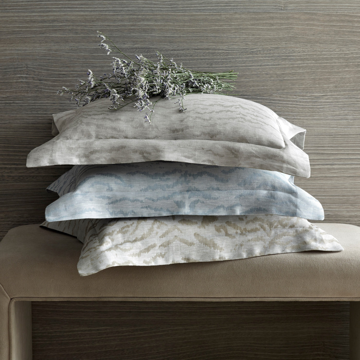 Three stacked Home Treasures Alina pillowcases in silver, mist blue, and champagne tones.