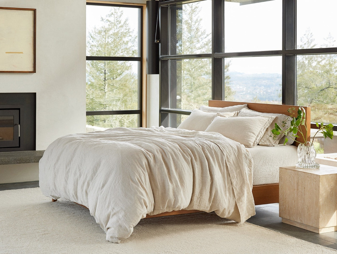 Ivory Coyuchi Relaxed Linen sheet set styled on bed in modern room with floor-to-ceiling windows.