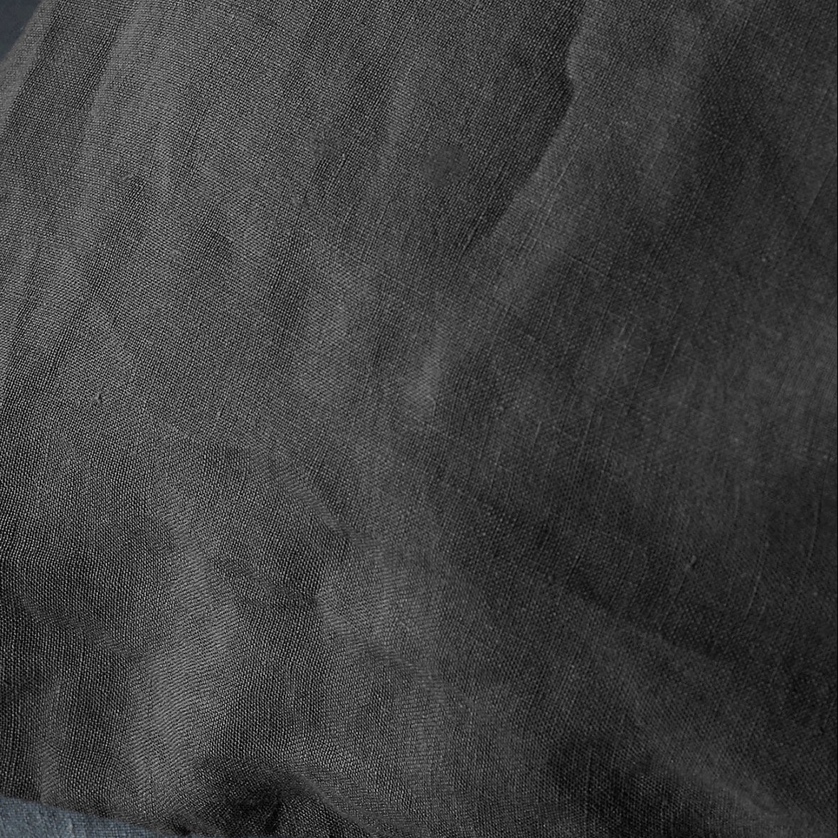 Close-up of charcoal washed linen fabric showing natural texture and soft drape.