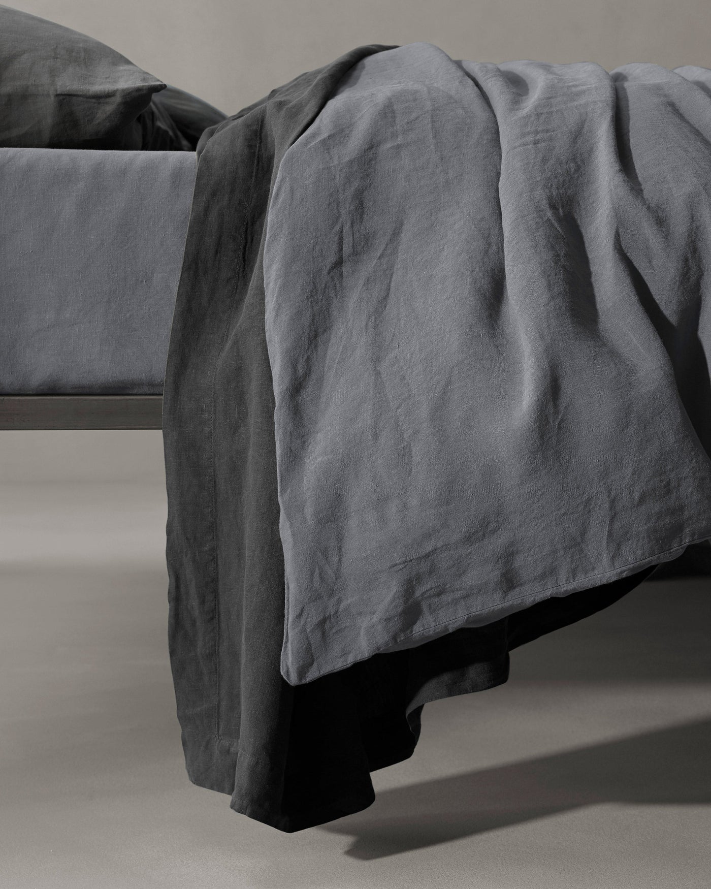 Charcoal linen duvet cover draped loosely over bed foot, showing natural texture.