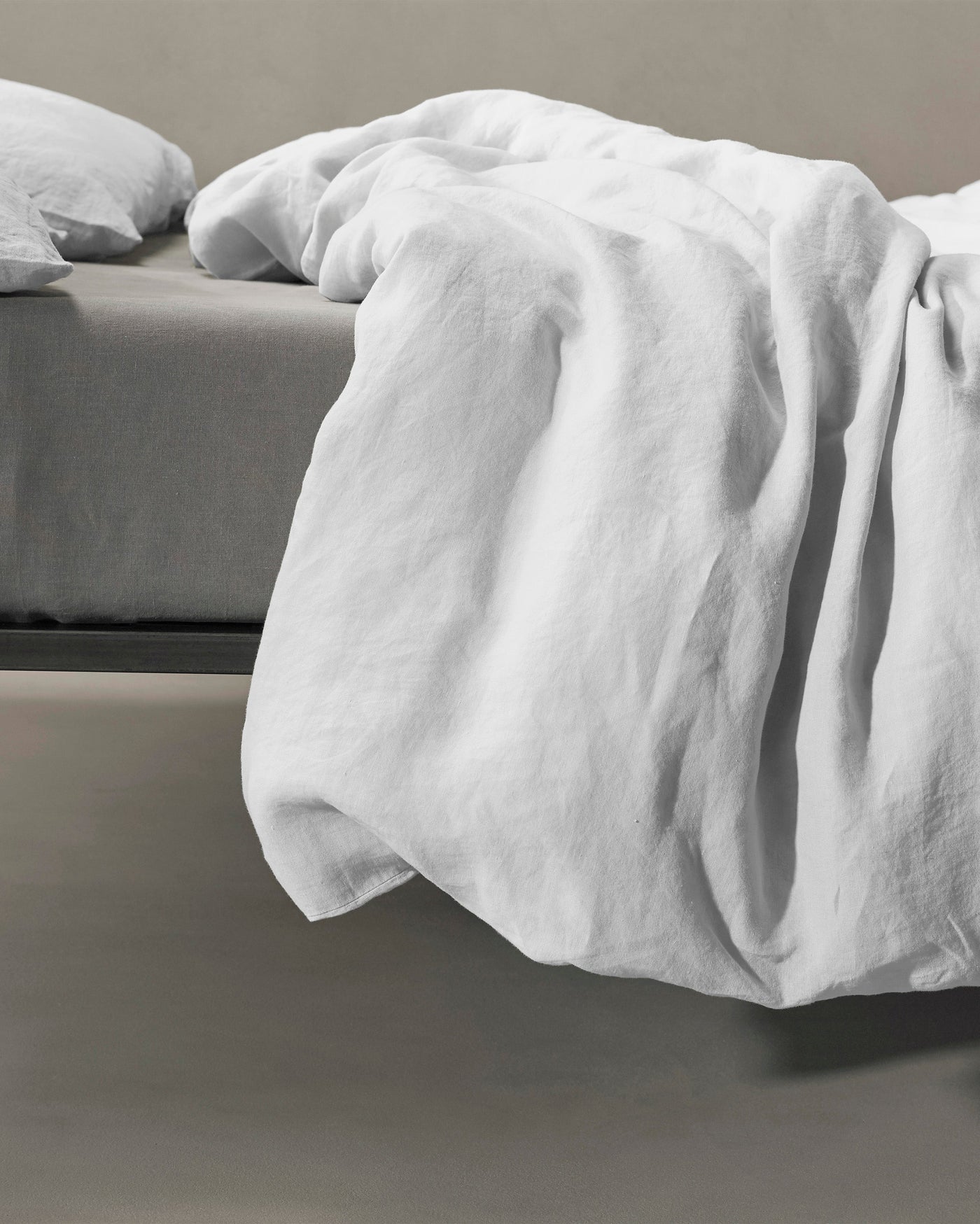 White linen duvet cover draped loosely over bed edge, showing relaxed texture.