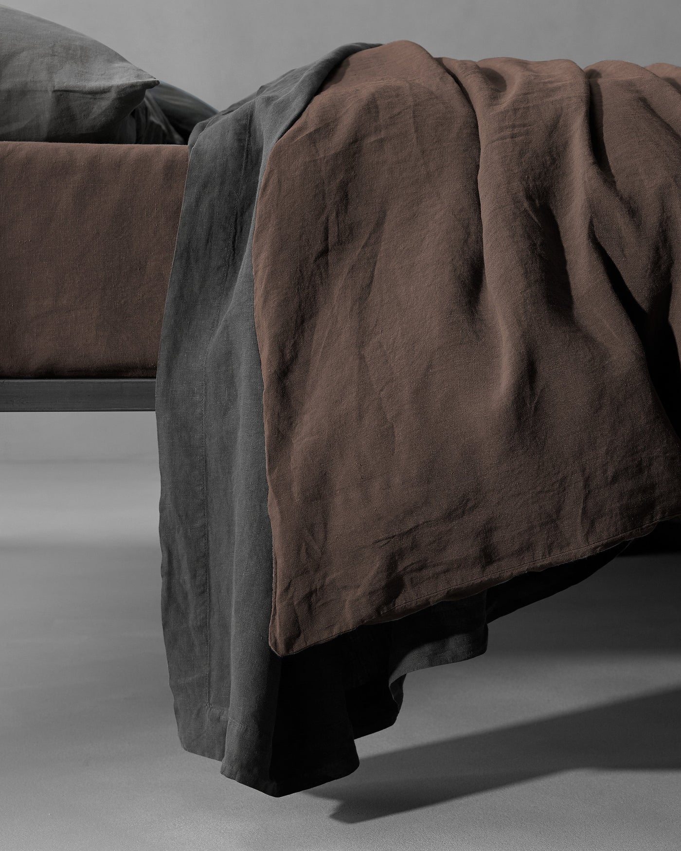 Close-up of Society Limonta Rem duvet cover draping over bed foot in espresso linen.