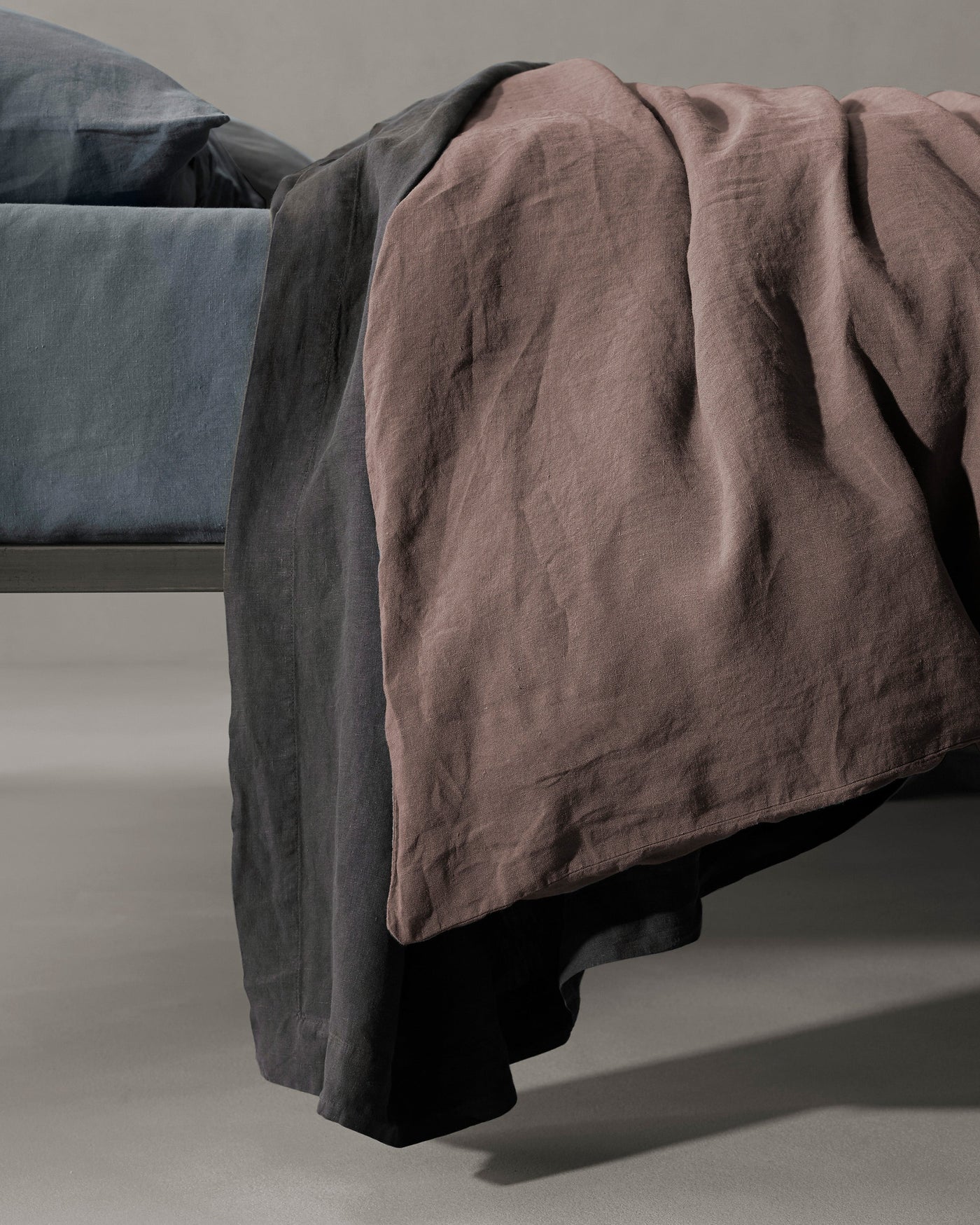 Society Limonta Rem duvet cover in mauve draped over charcoal linen bedding.