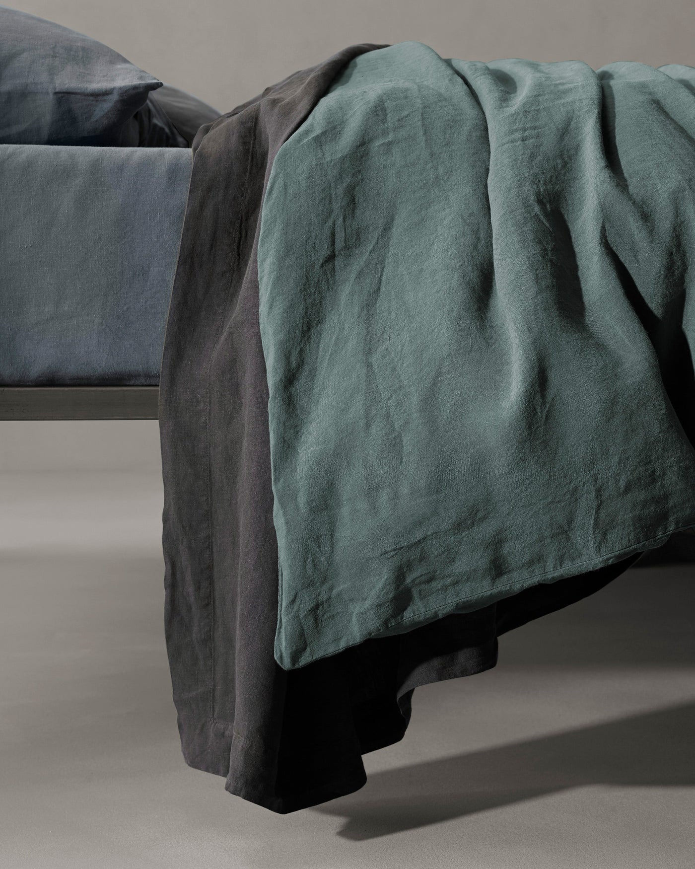 Teal linen duvet draped over charcoal bedding, showing textured weave at foot of bed.