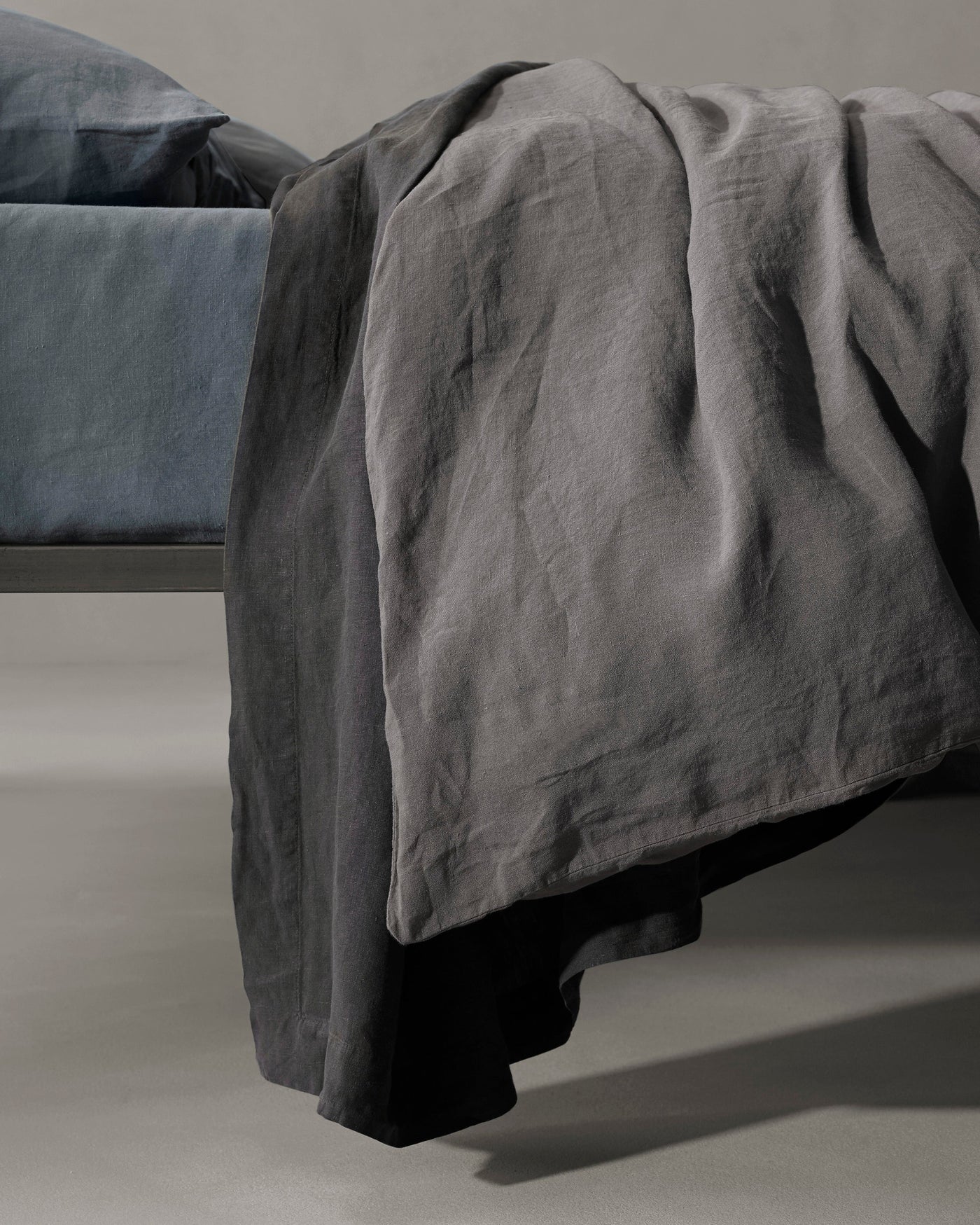 Society Limonta Rem duvet cover in graphite linen, draped over bed foot showing natural texture.