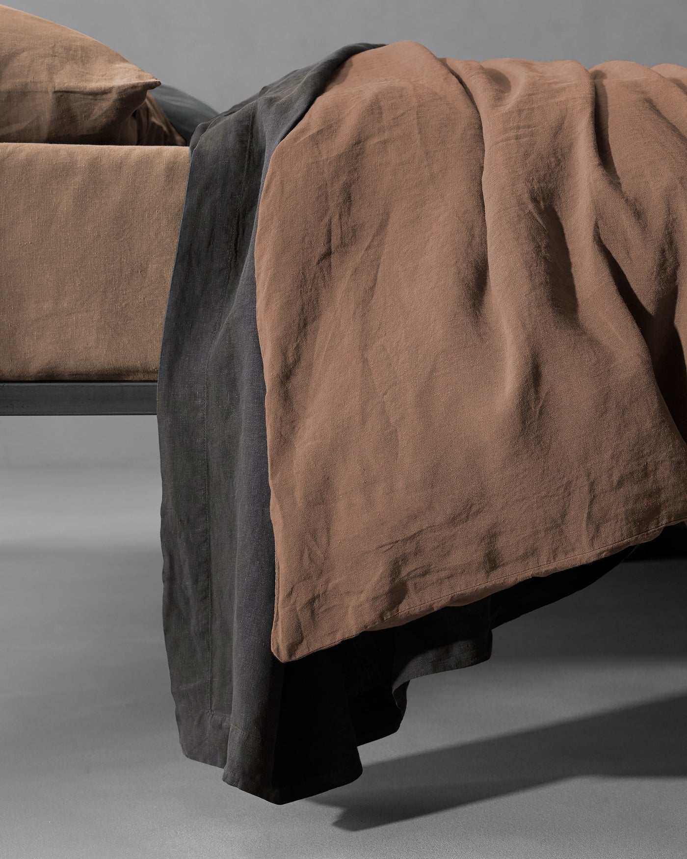 Charcoal linen reverse visible as tobacco duvet cover drapes over foot of bed.