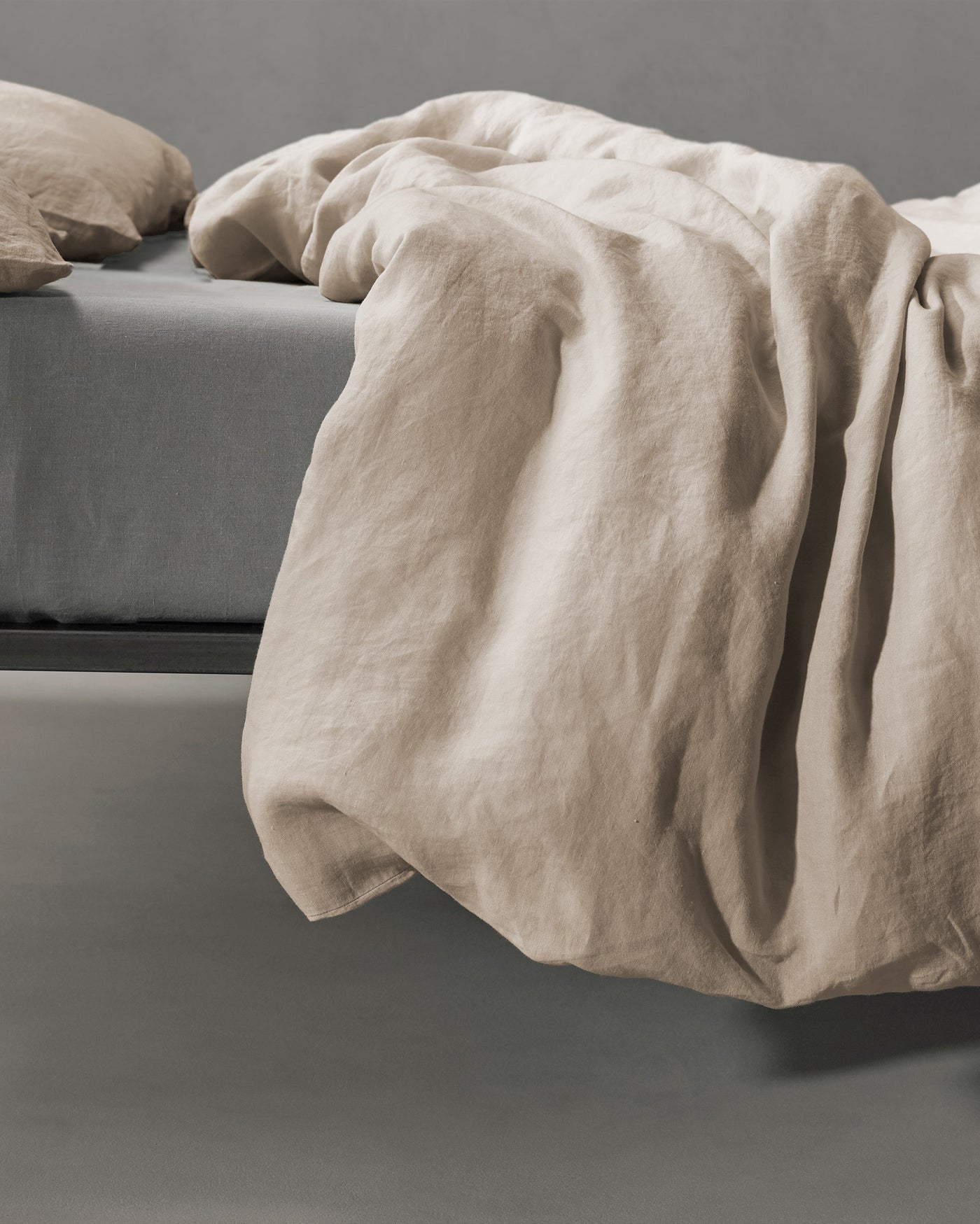 Sand-toned linen duvet cover draped loosely over a bed edge, showing natural texture.