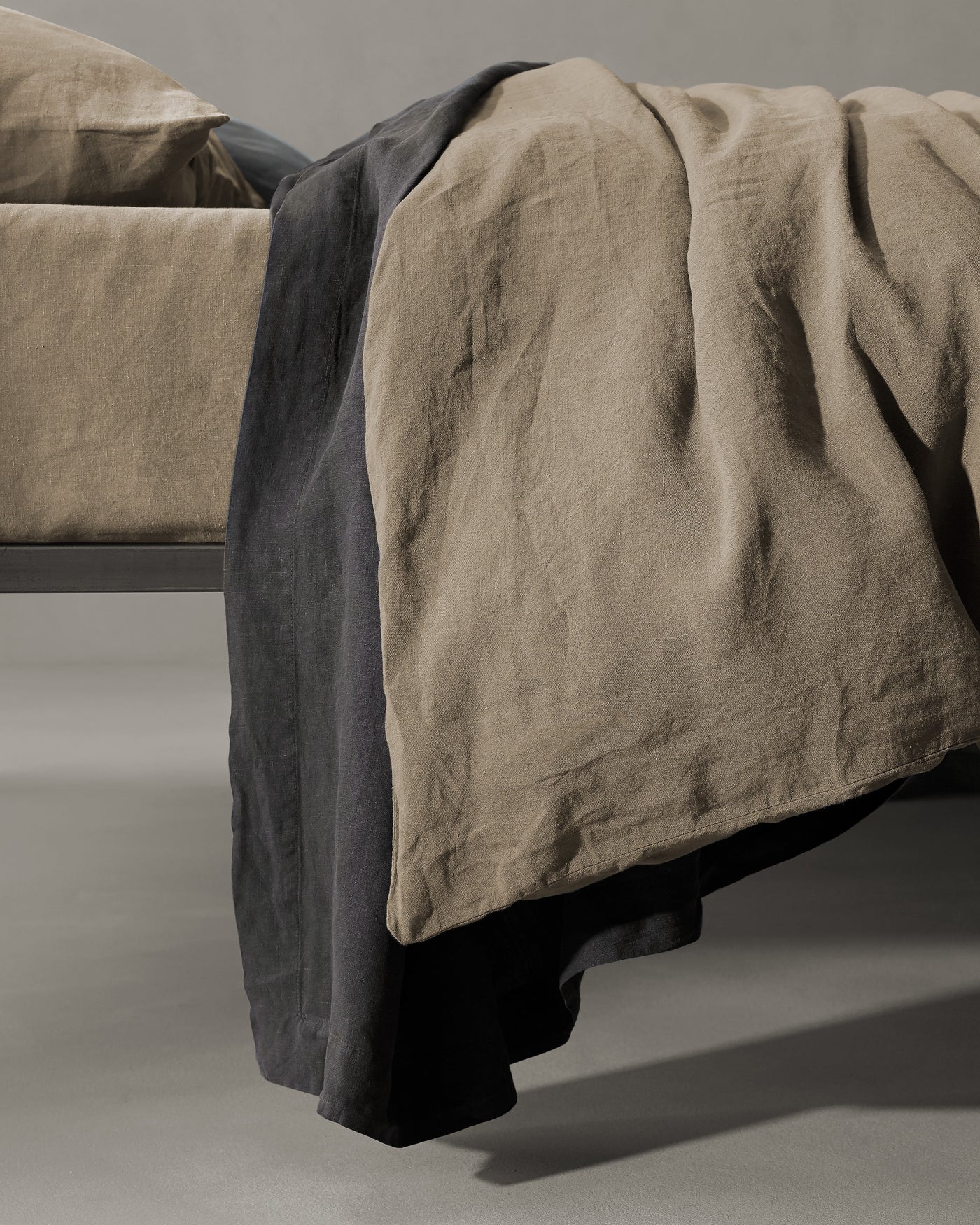 Draped foot-of-bed view showing taupe and charcoal linen contrast layers cascading to the floor.