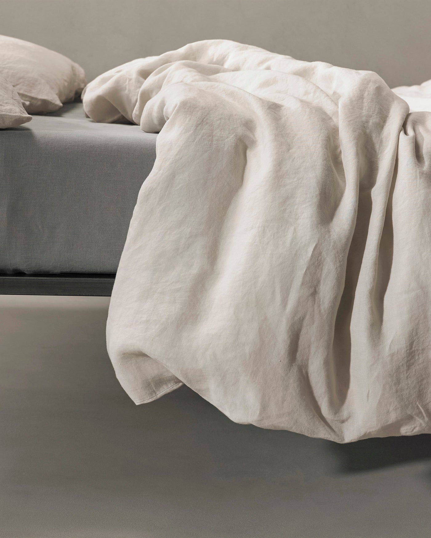 Society Limonta Rem duvet cover in ivory linen, draped loosely over bed edge.