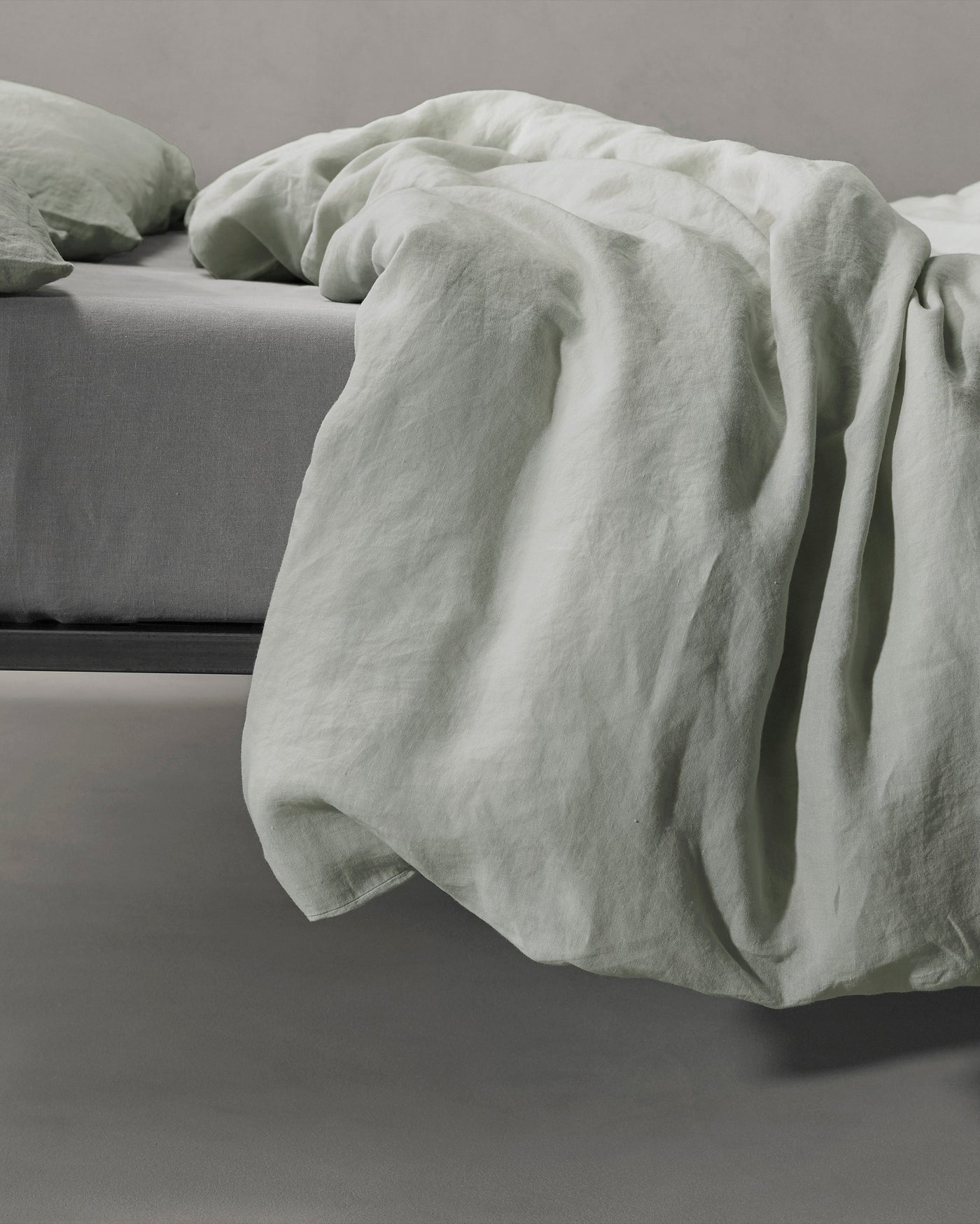Sage linen duvet cover draped loosely over bed edge, showing relaxed texture.