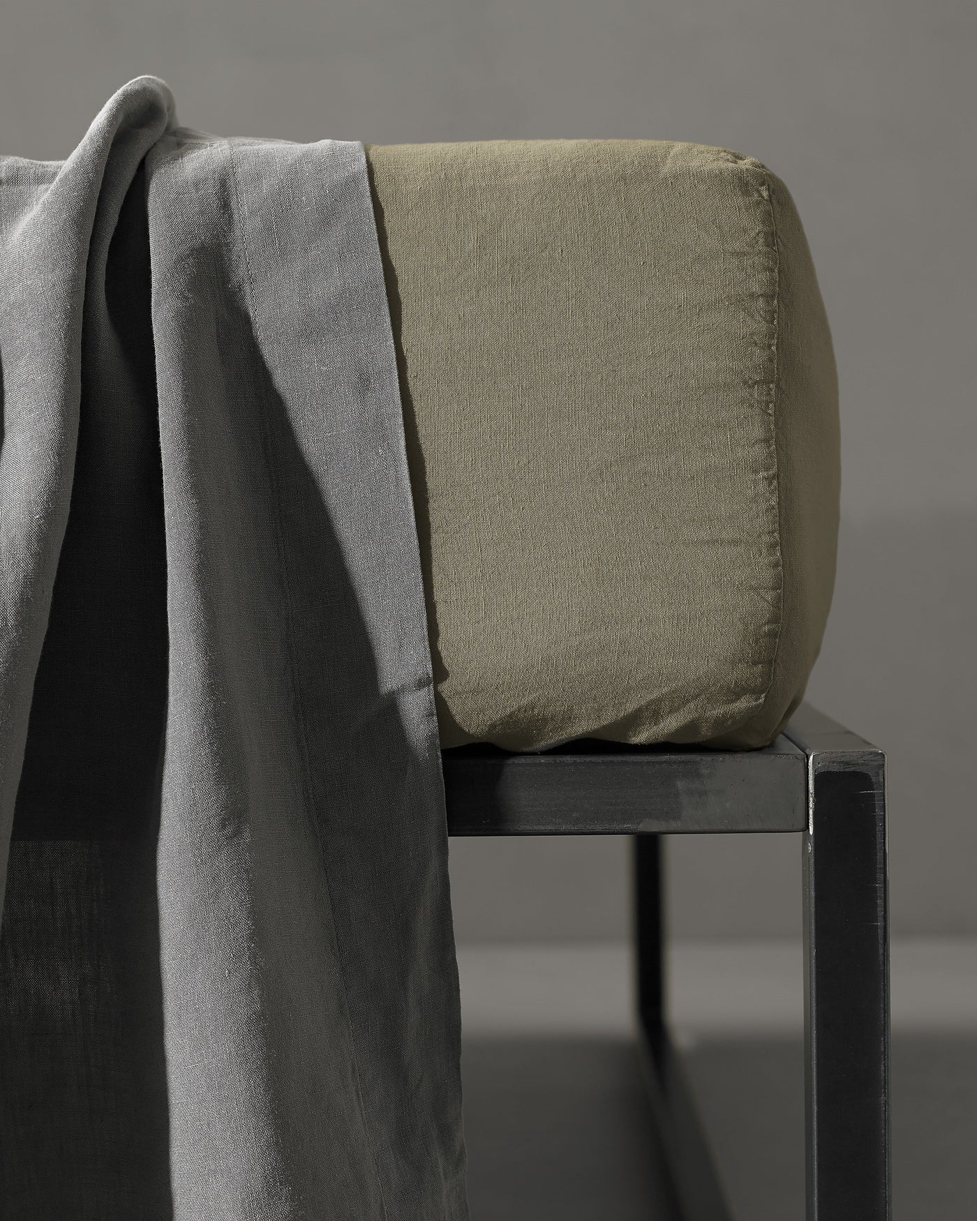Sage fitted sheet corner detail showing structured drape over dark metal bench with slate throw.