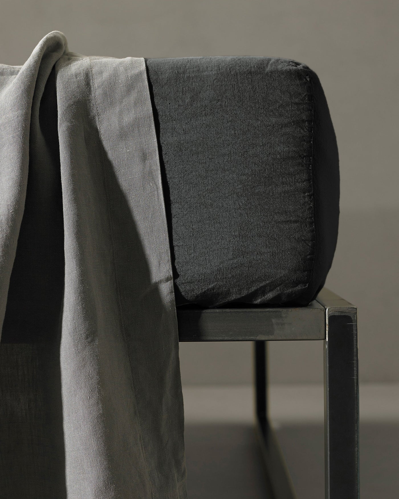 Charcoal fitted sheet corner detail on a chair with a silver-grey linen drape.