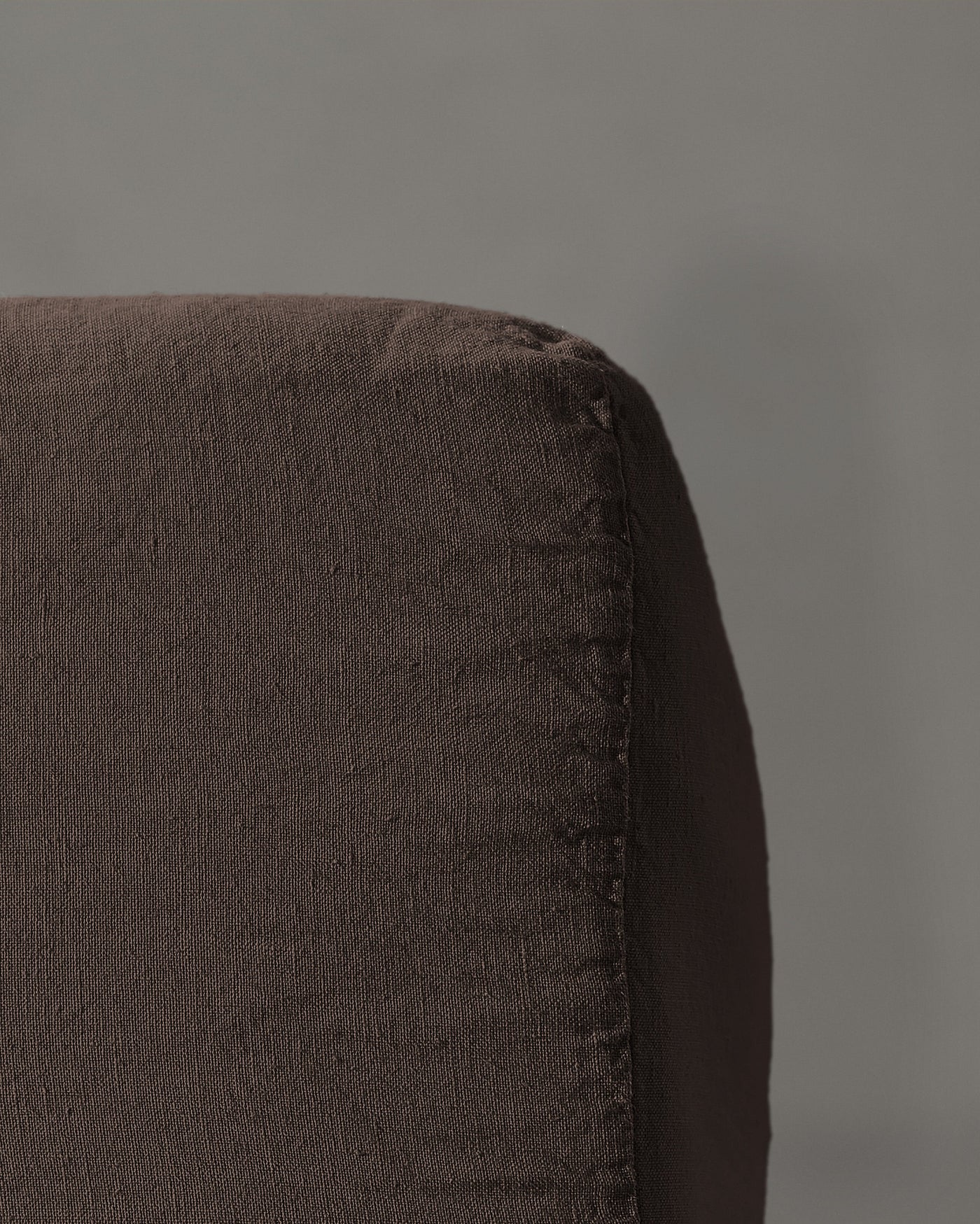 Close-up of espresso linen fitted sheet corner showing textured weave and stitched edge.