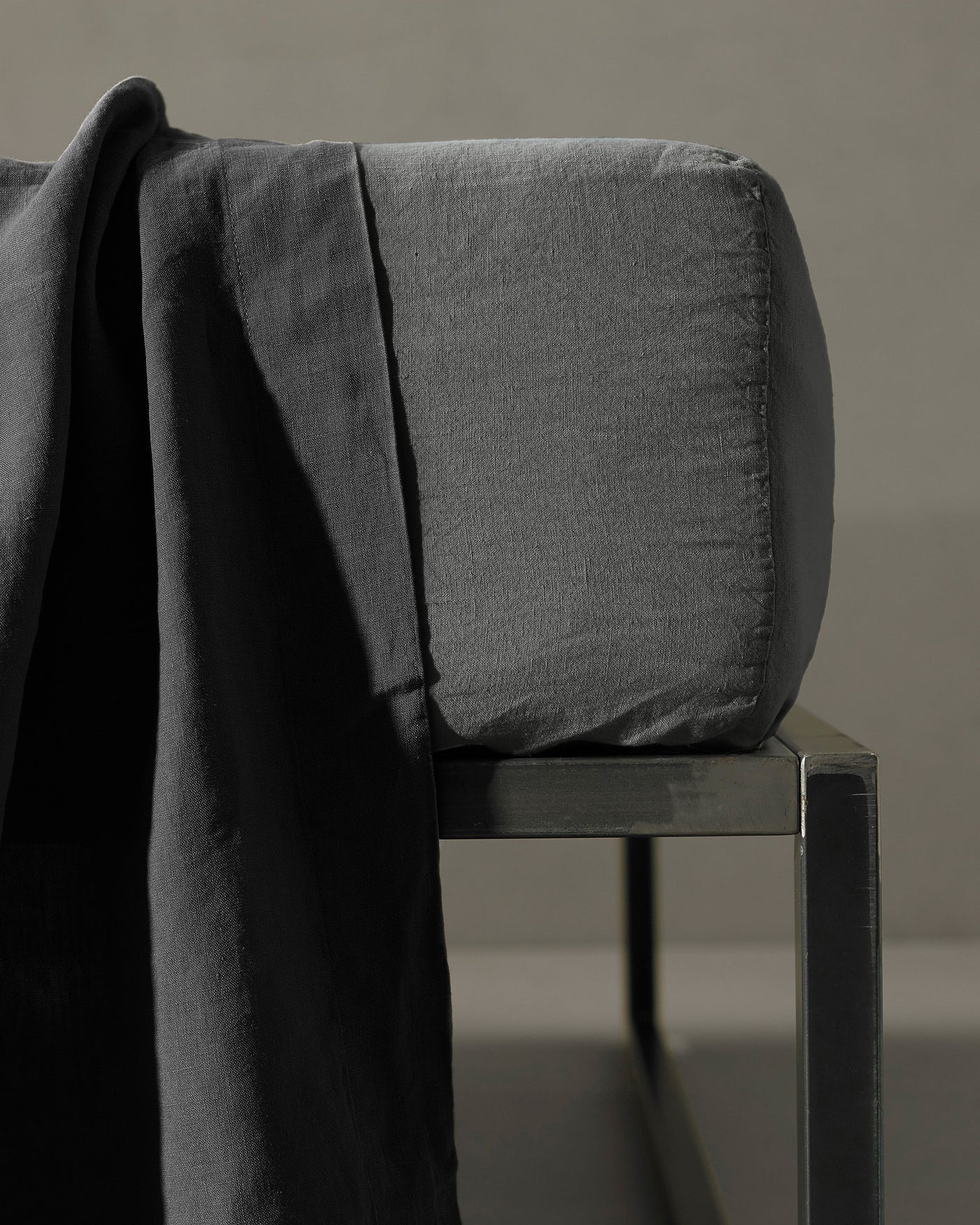 Charcoal fitted sheet draped over a dark metal chair, showing fabric texture and depth.