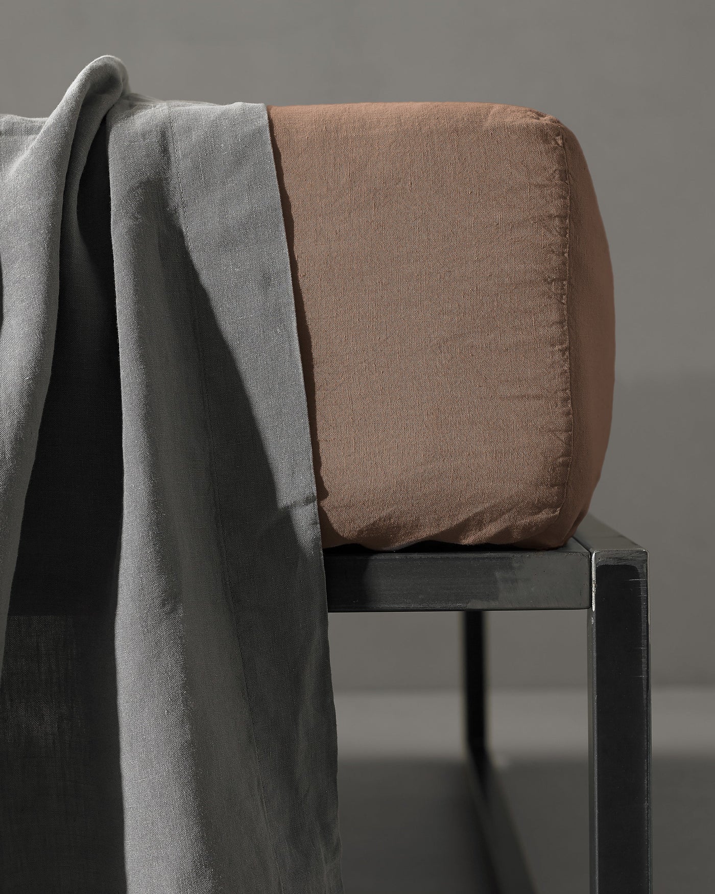Tobacco fitted sheet corner detail draped over black bench with grey linen throw.