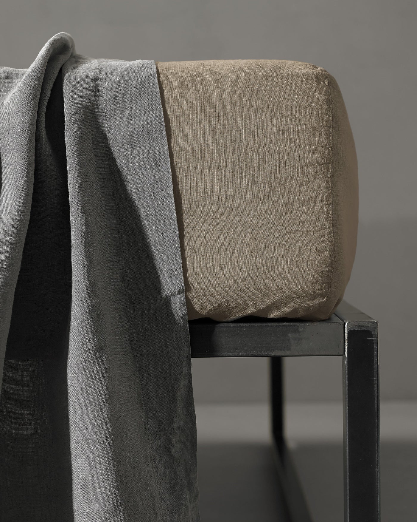Taupe fitted sheet wrapped over a cushion beside a draped slate linen throw.