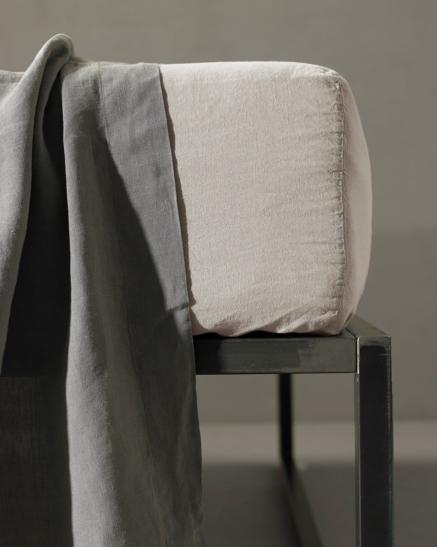 Dove grey linen fitted sheet draped over a dark chair, textured weave visible.