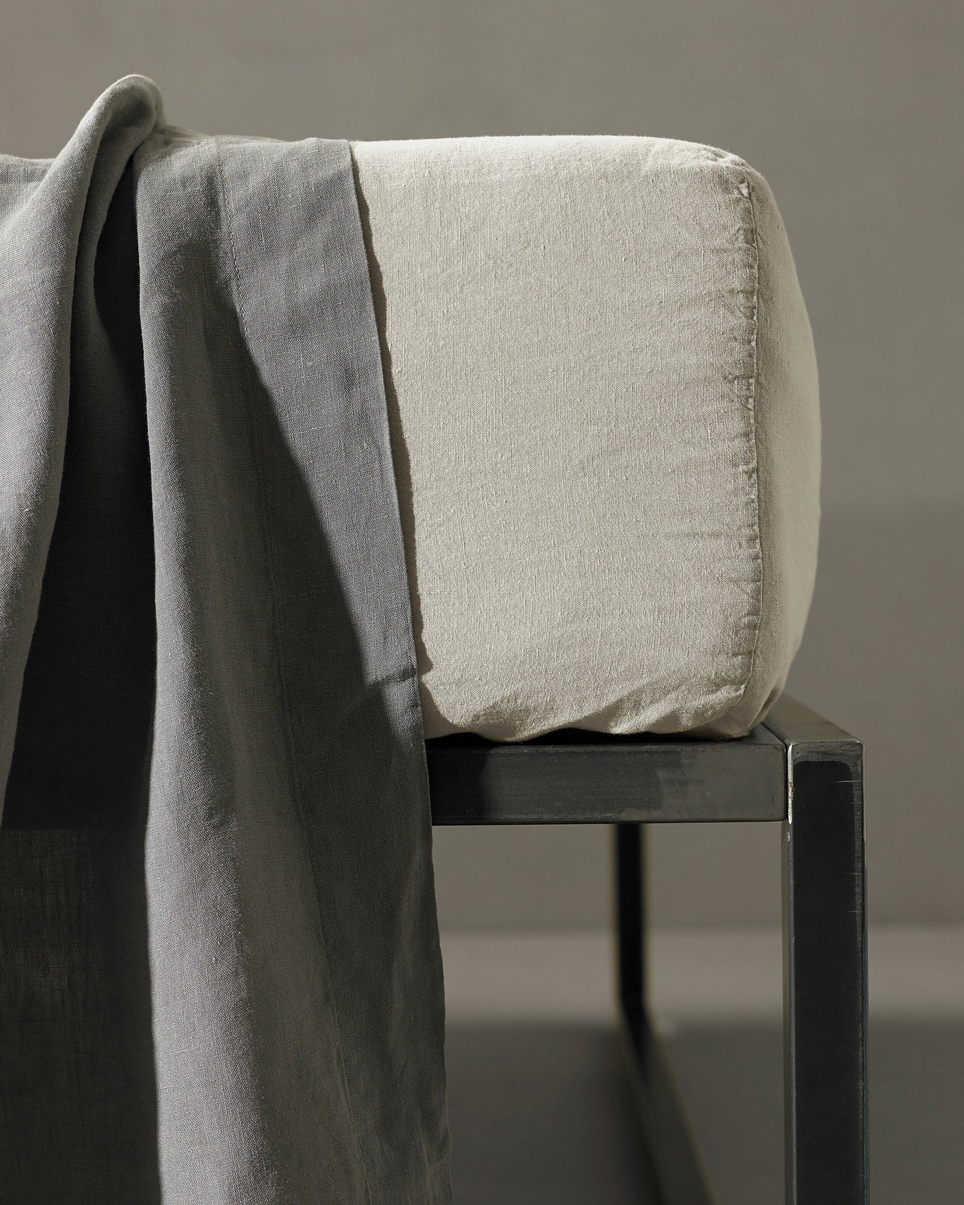 Close-up of ivory linen fitted sheet corner on a chair, draped grey fabric alongside.