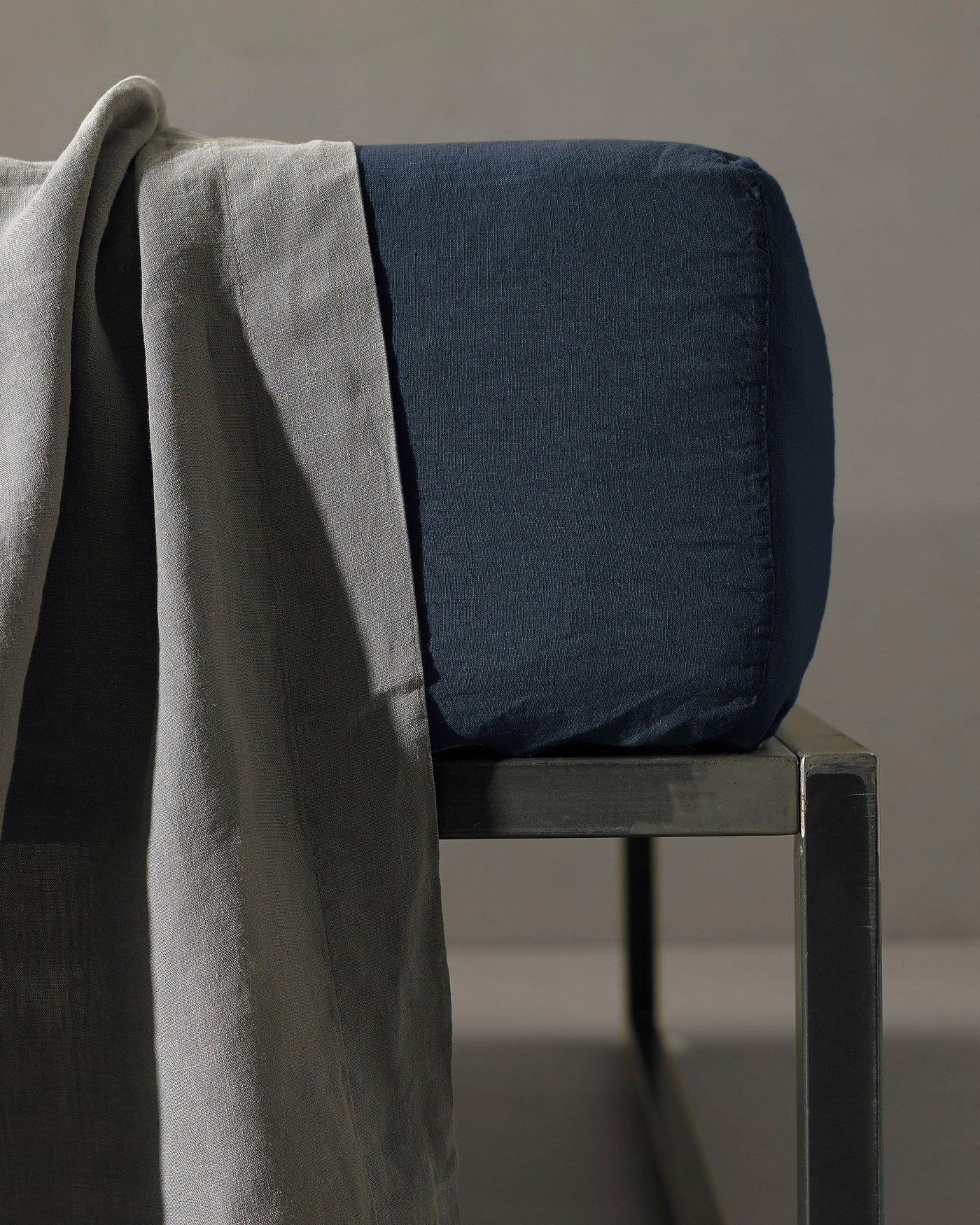 Navy fitted sheet corner detail on a metal chair, with a grey linen throw draped alongside.