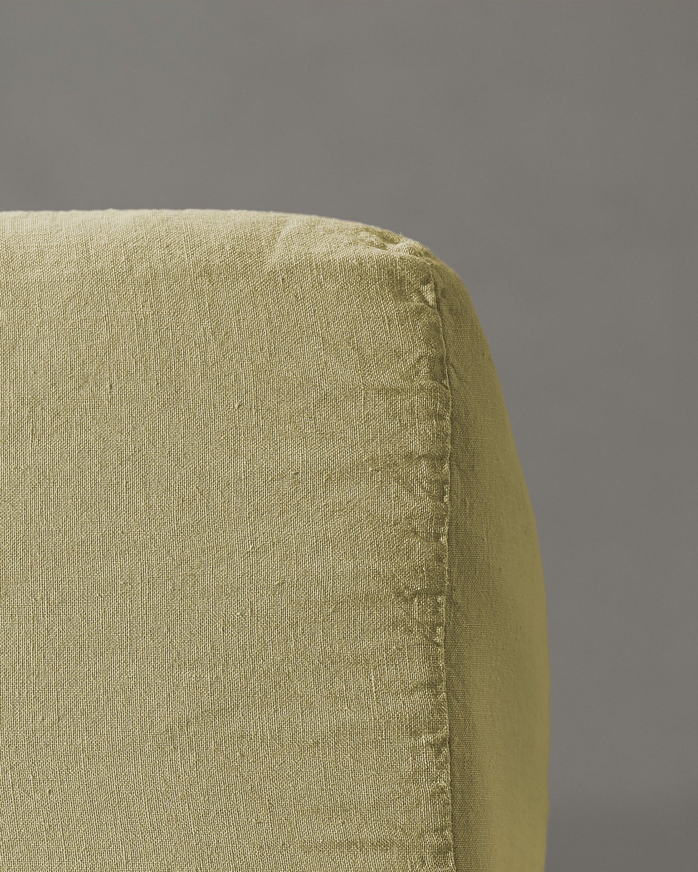 Close-up of sage linen fitted sheet corner seam detail against grey background.