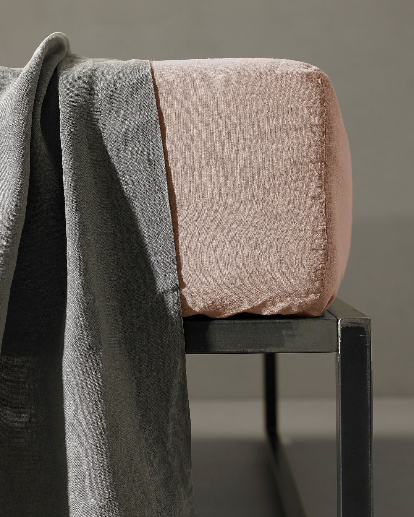 Society Limonta Rem blush fitted sheet corner on dark stool with grey draped sheet.