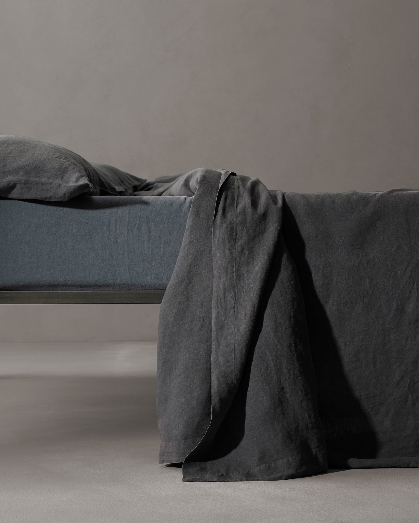 Charcoal linen flat sheet draped over bed edge, showing relaxed drape and texture.