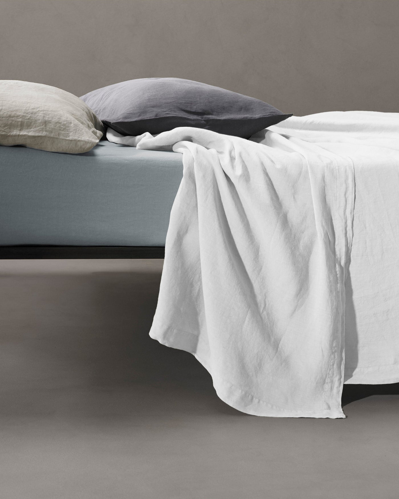 White linen flat sheet draped loosely over the edge of a bed.