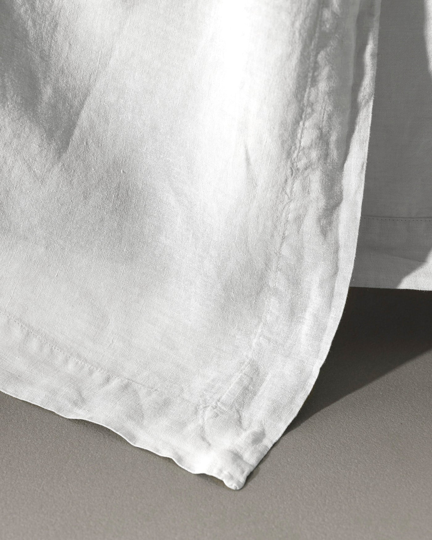 Close-up of white washed linen flat sheet hem with natural texture in soft shadow.