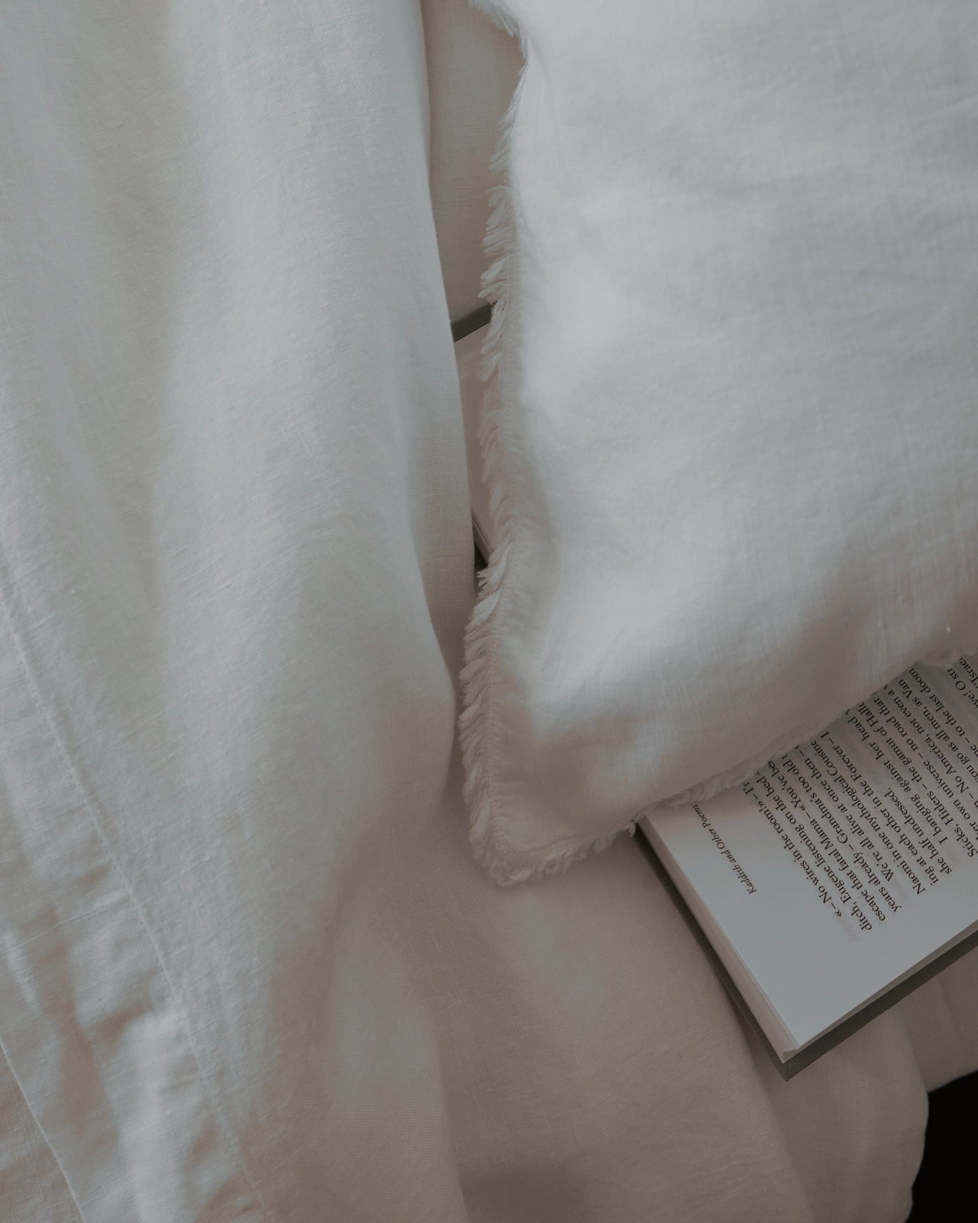 Close-up of ivory Society Limonta Rem linen flat sheet fringe edge with open book.