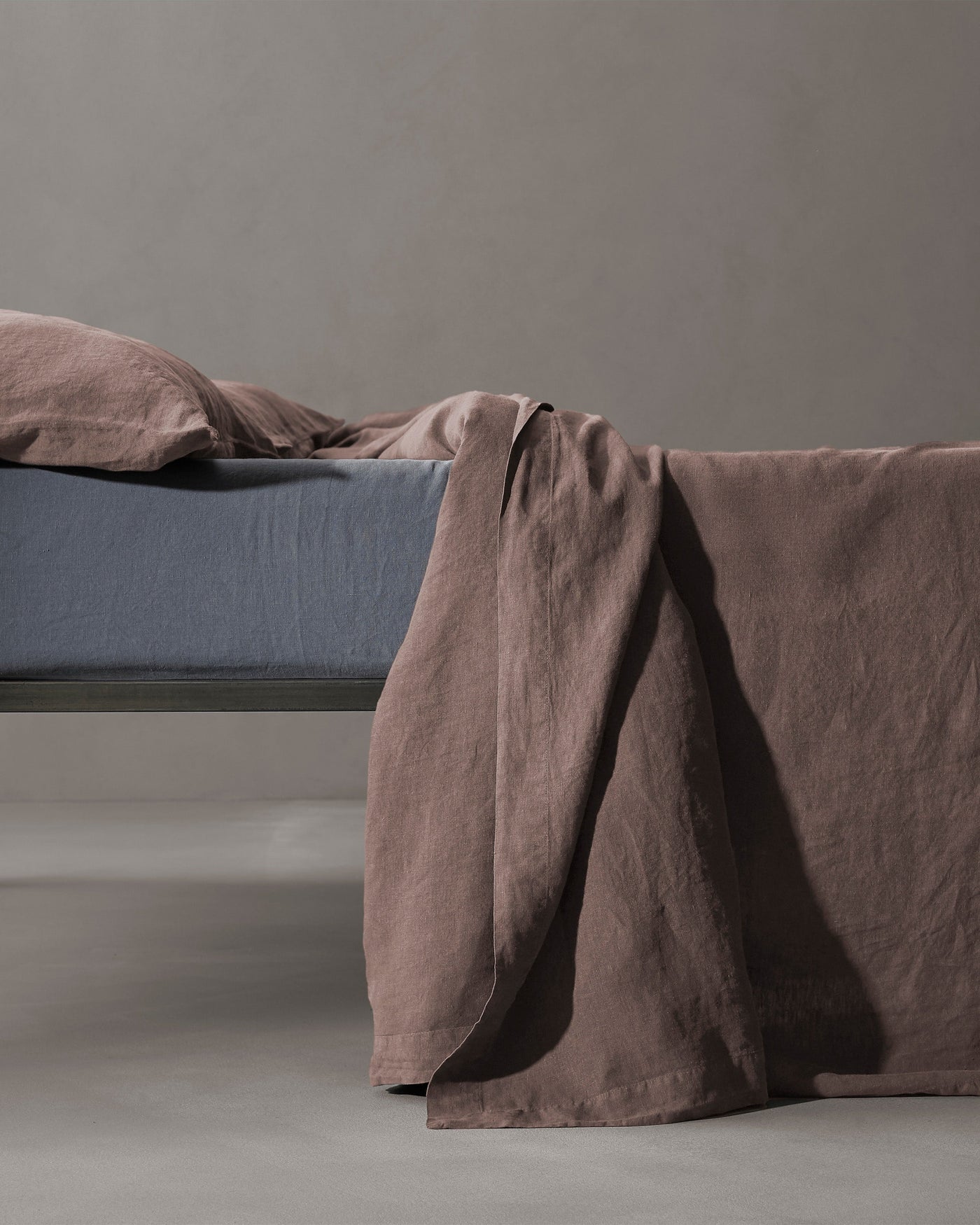 Society Limonta Rem flat sheet in mauve linen draped over bed edge.