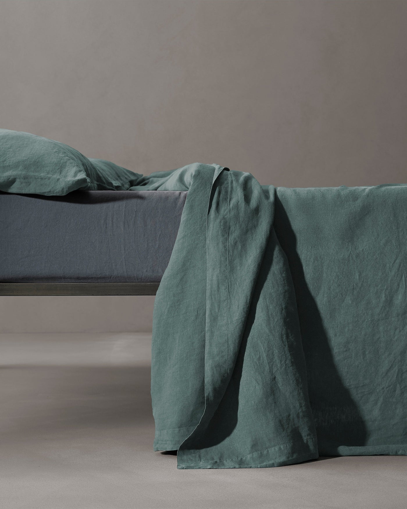Society Limonta Rem flat sheet in teal linen, draped over bed edge showing relaxed texture.