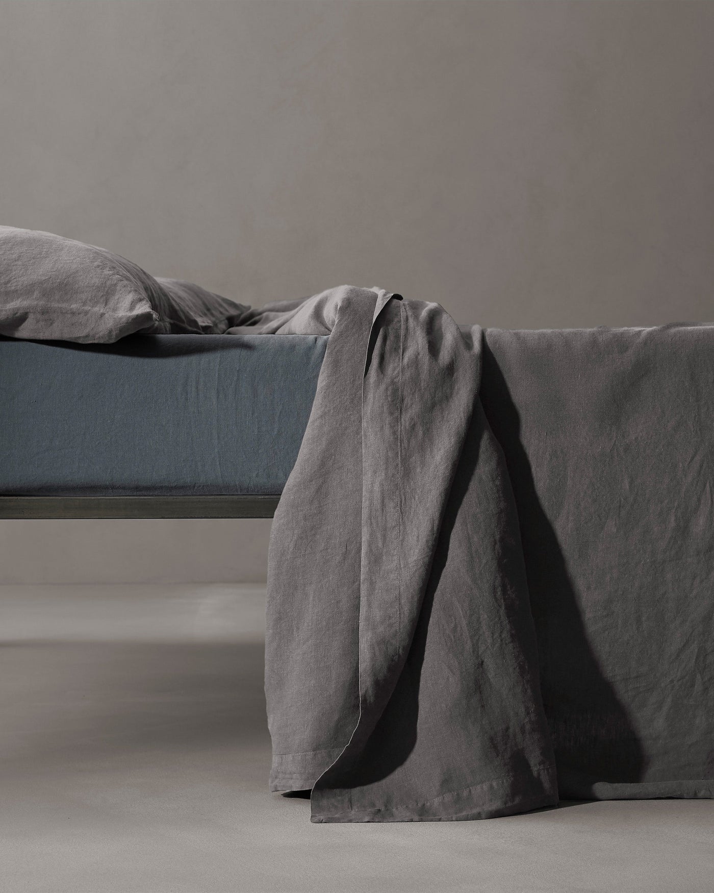 Charcoal linen flat sheet draped over bed edge, showing natural texture and relaxed drape.