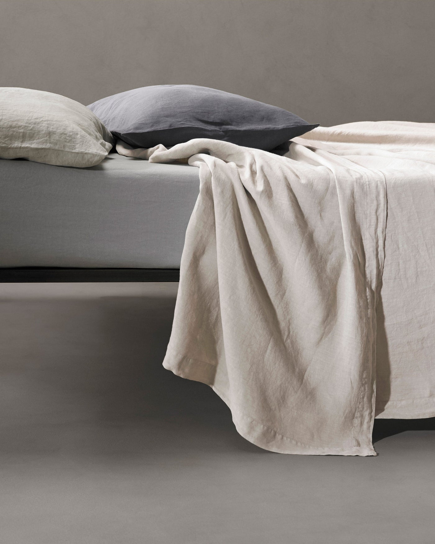 Ivory linen flat sheet draped loosely over the edge of a bed.