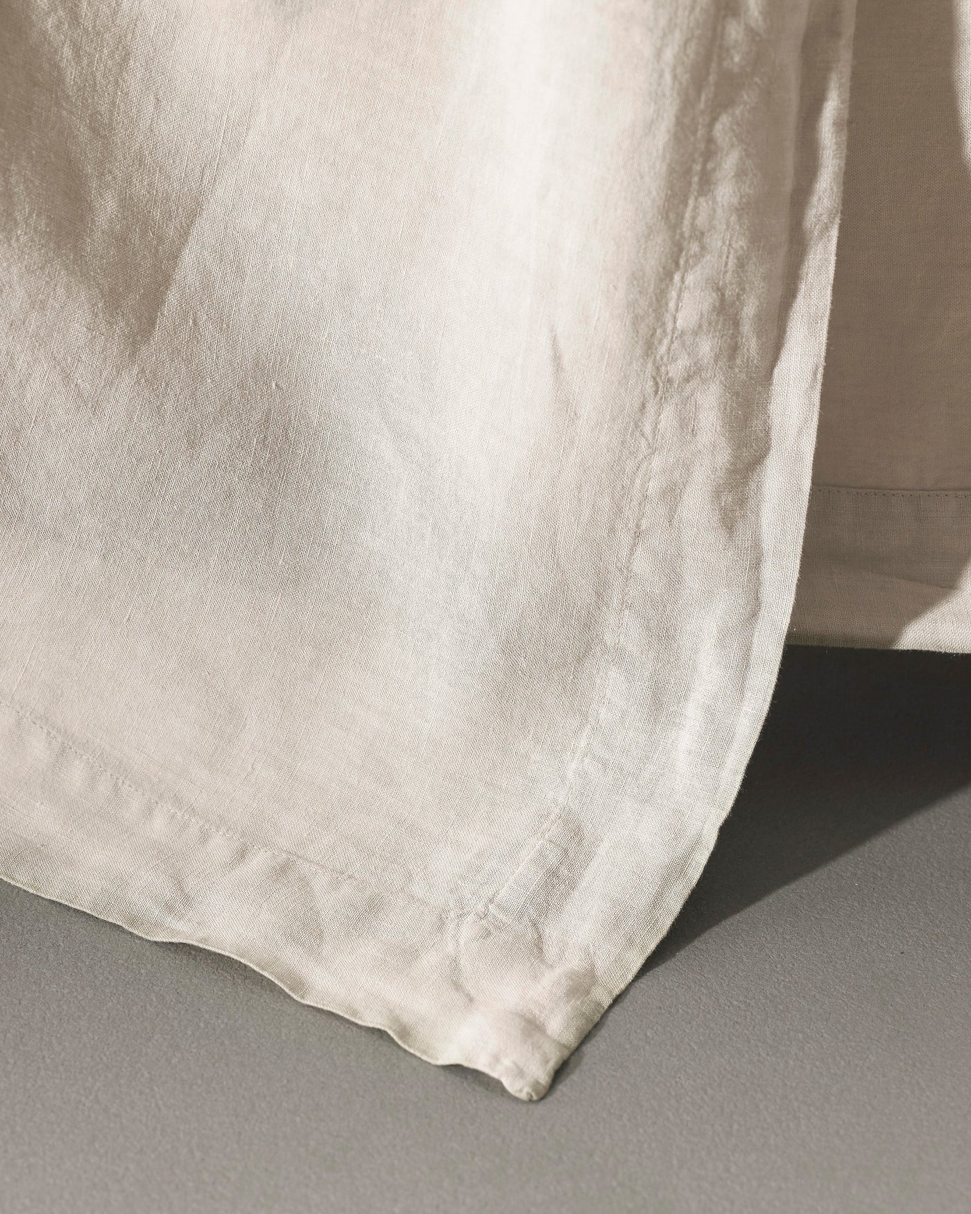 Close-up of ivory washed linen flat sheet hem, showing texture and stitched edge detail.