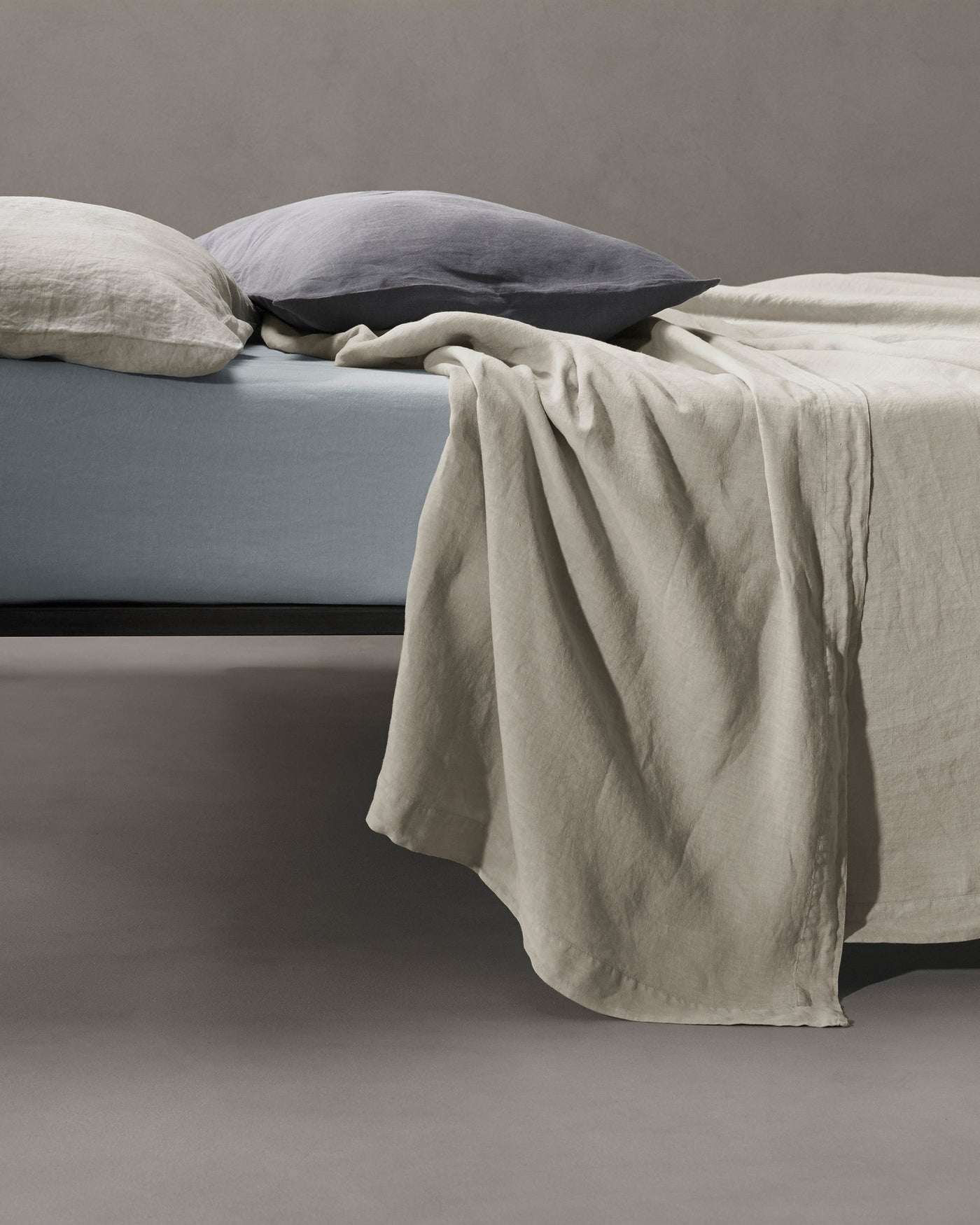 Society Limonta Rem flat sheet in sand linen draped over the foot of a styled bed.