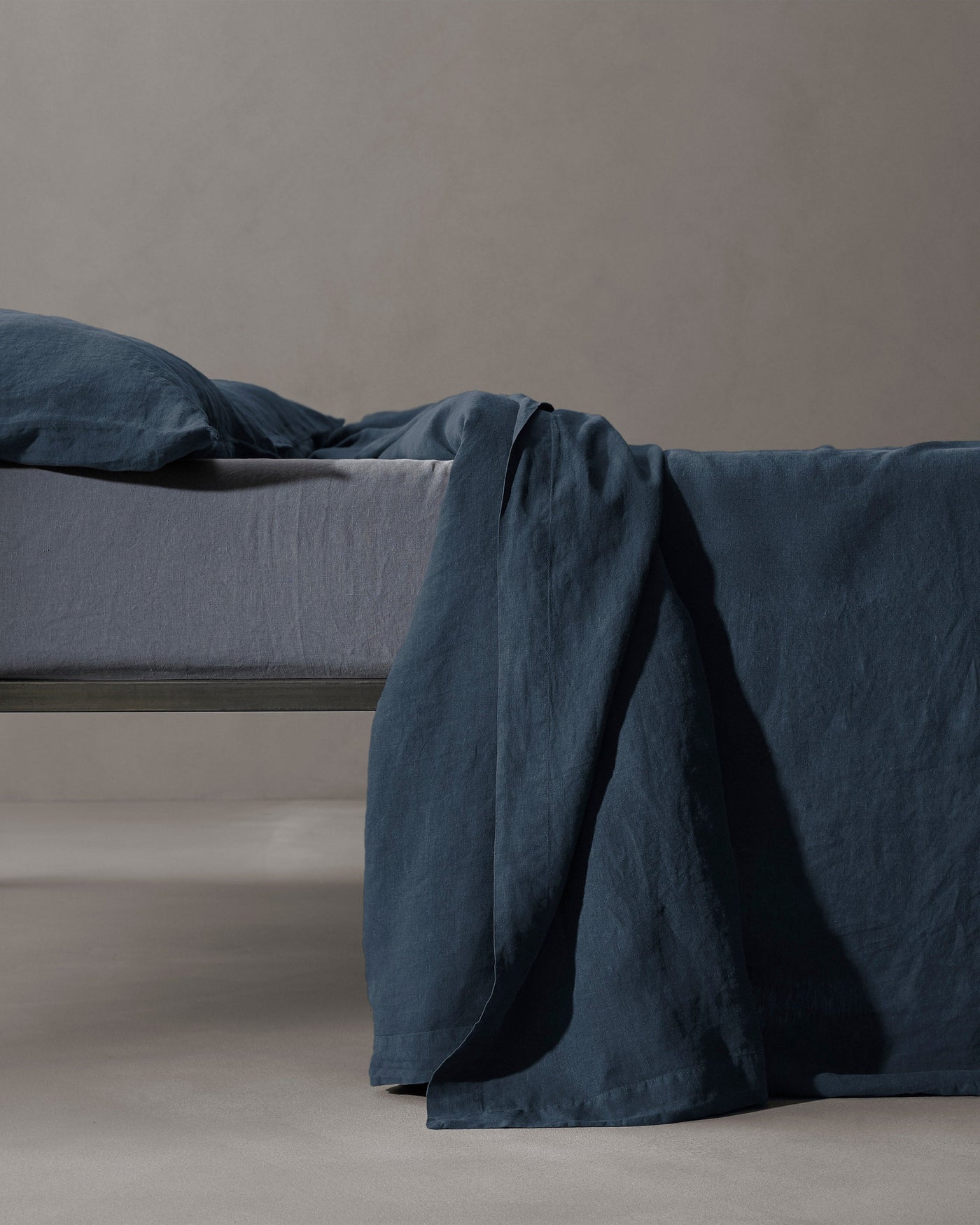 Society Limonta Rem flat sheet in ink blue linen draped over bed edge.